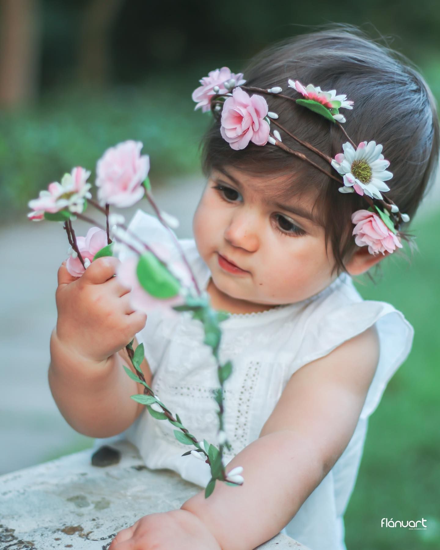 Adorable toddler girl with pink flower crown holding delicate floral branches outdoors.