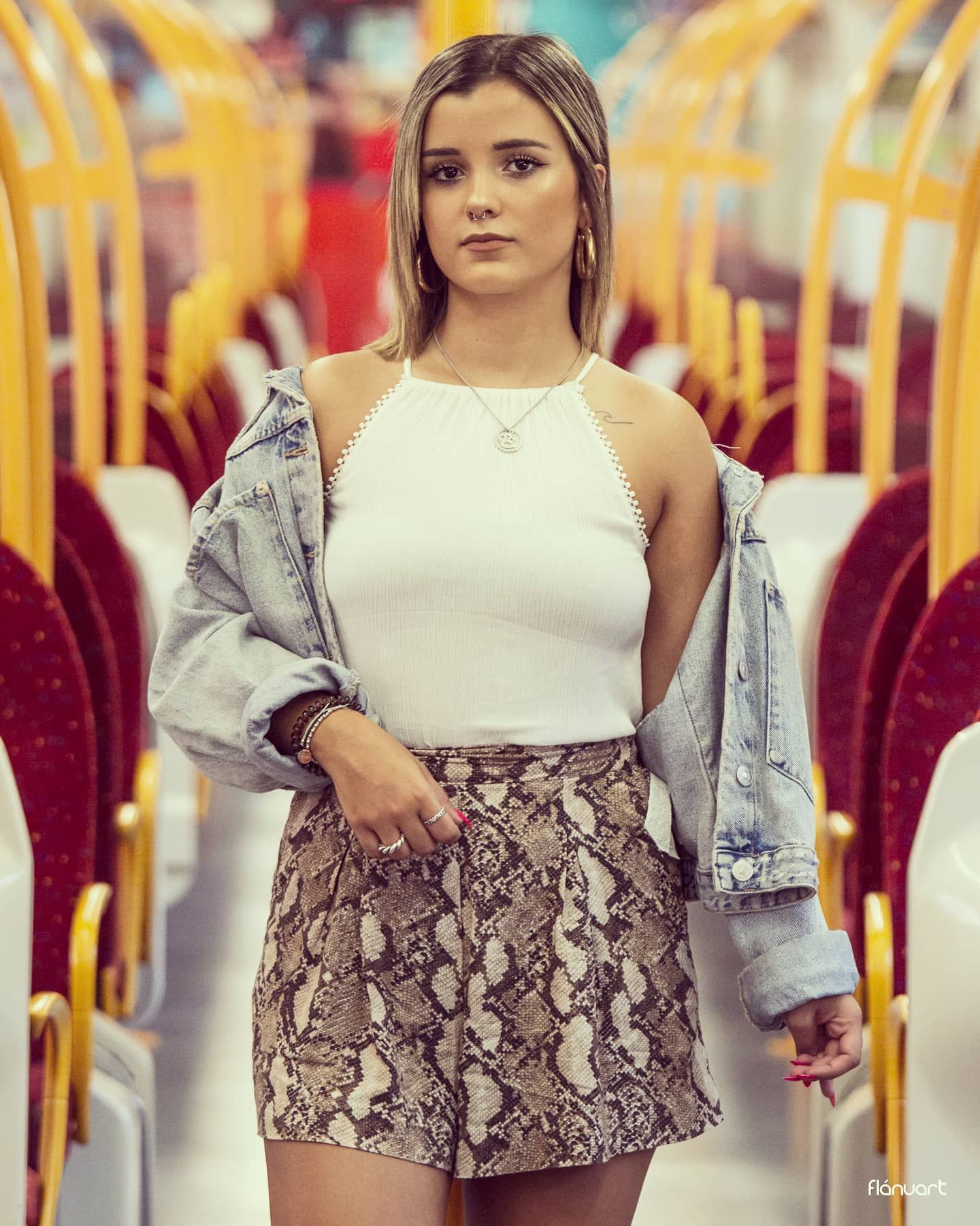 Young woman in white halter top, snake print skirt, and denim jacket poses inside a train.