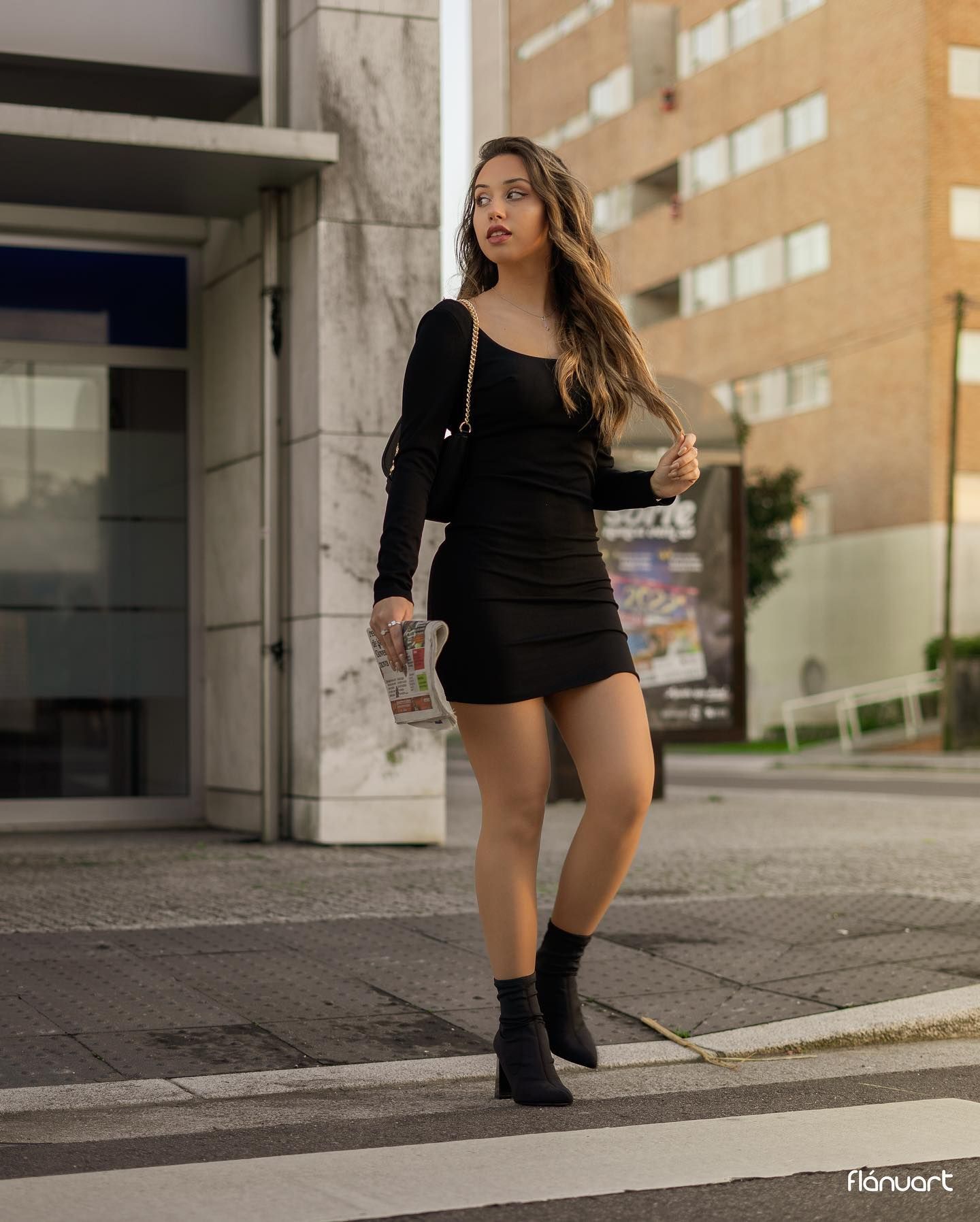 Young woman in all-black outfit with mini skirt and ankle boots walks on a city street.