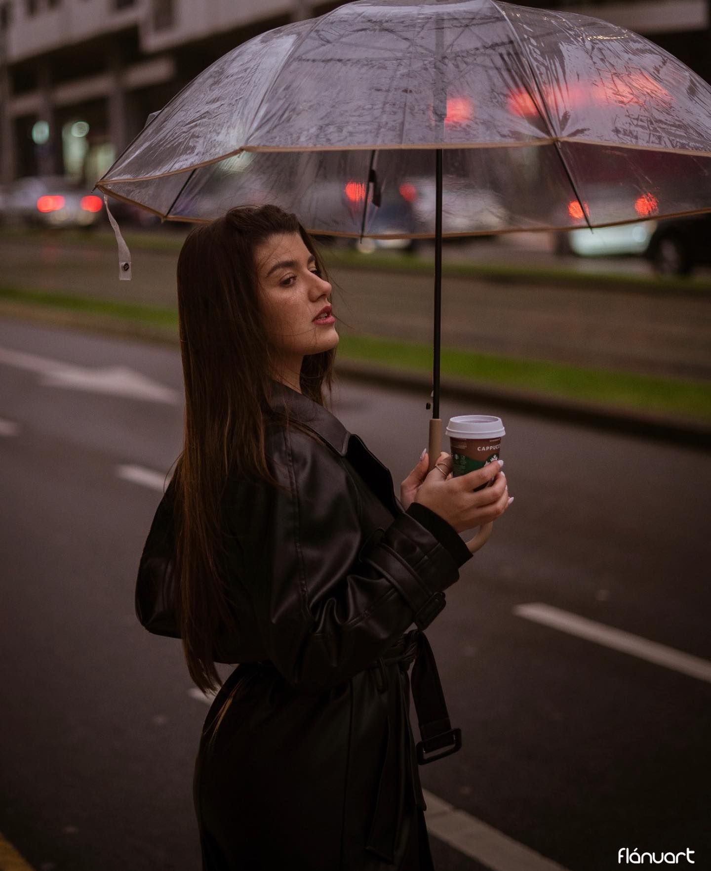 Woman holding umbrella and coffee cup on rainy city street at night.