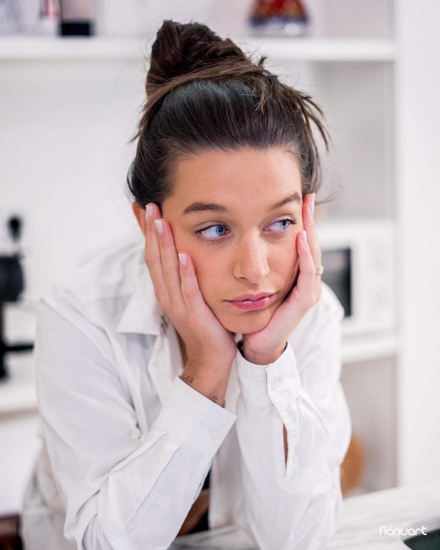 Young woman with hair in bun resting face in hands with thoughtful expression indoors.