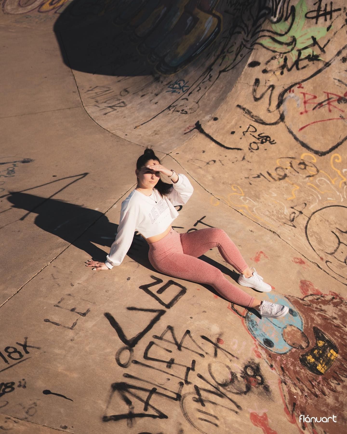 Woman in pink leggings sitting in a graffiti-covered skate park bowl with a skateboard.