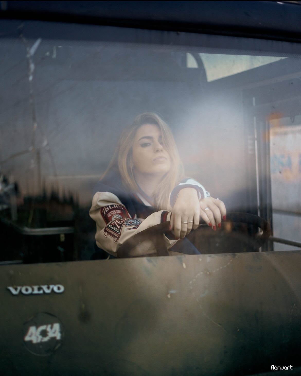 Young woman sitting inside a vintage Volvo vehicle, photographed through the window with moody cinematic lighting.