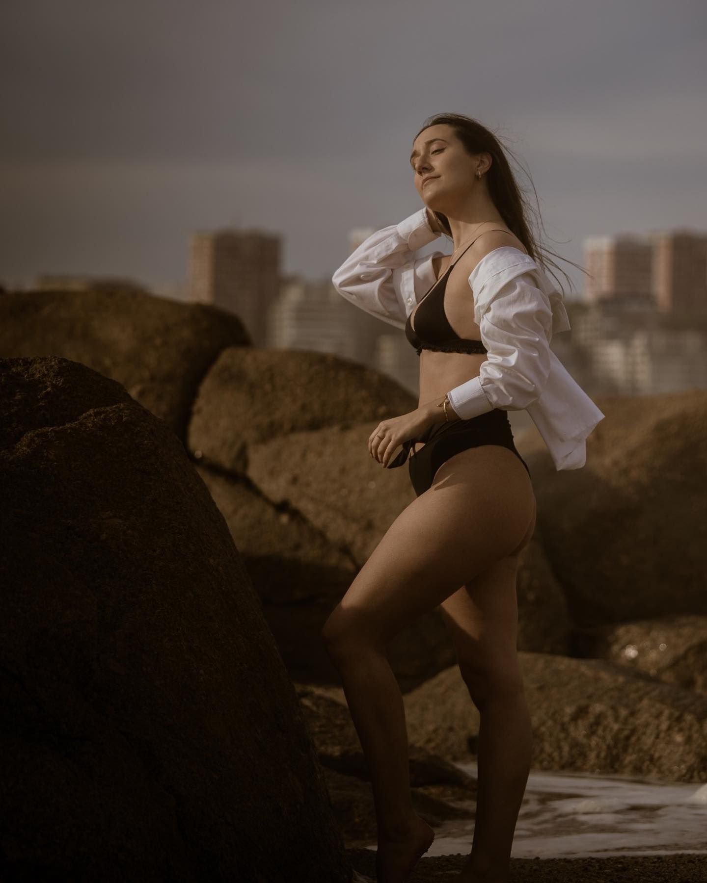 Woman in black bikini and white shirt posing on rocks.