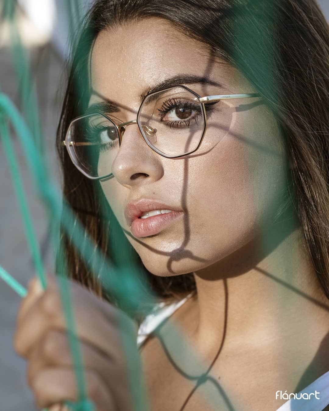 Close-up portrait of a brunette woman wearing round glasses with green rope shadows across her face.