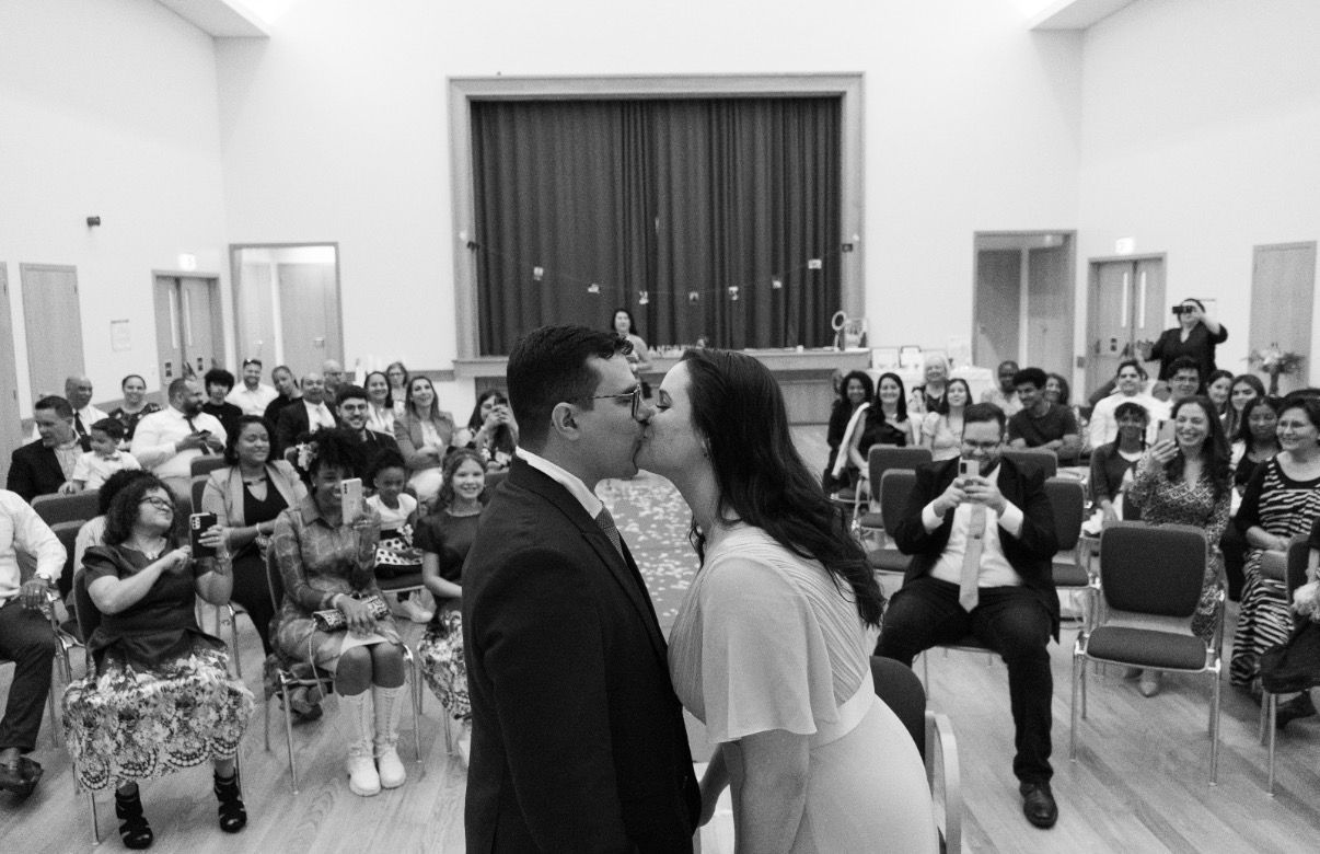 Newlyweds share a first kiss at the altar as wedding guests celebrate in black and white.