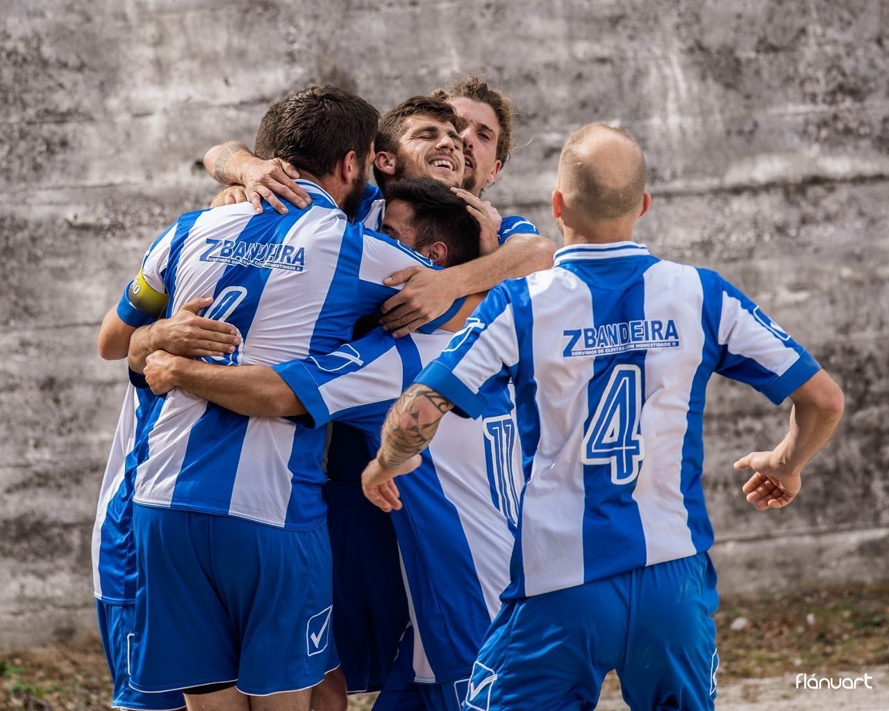 Football team celebrating a goal together on the field wearing blue and white jerseys.
