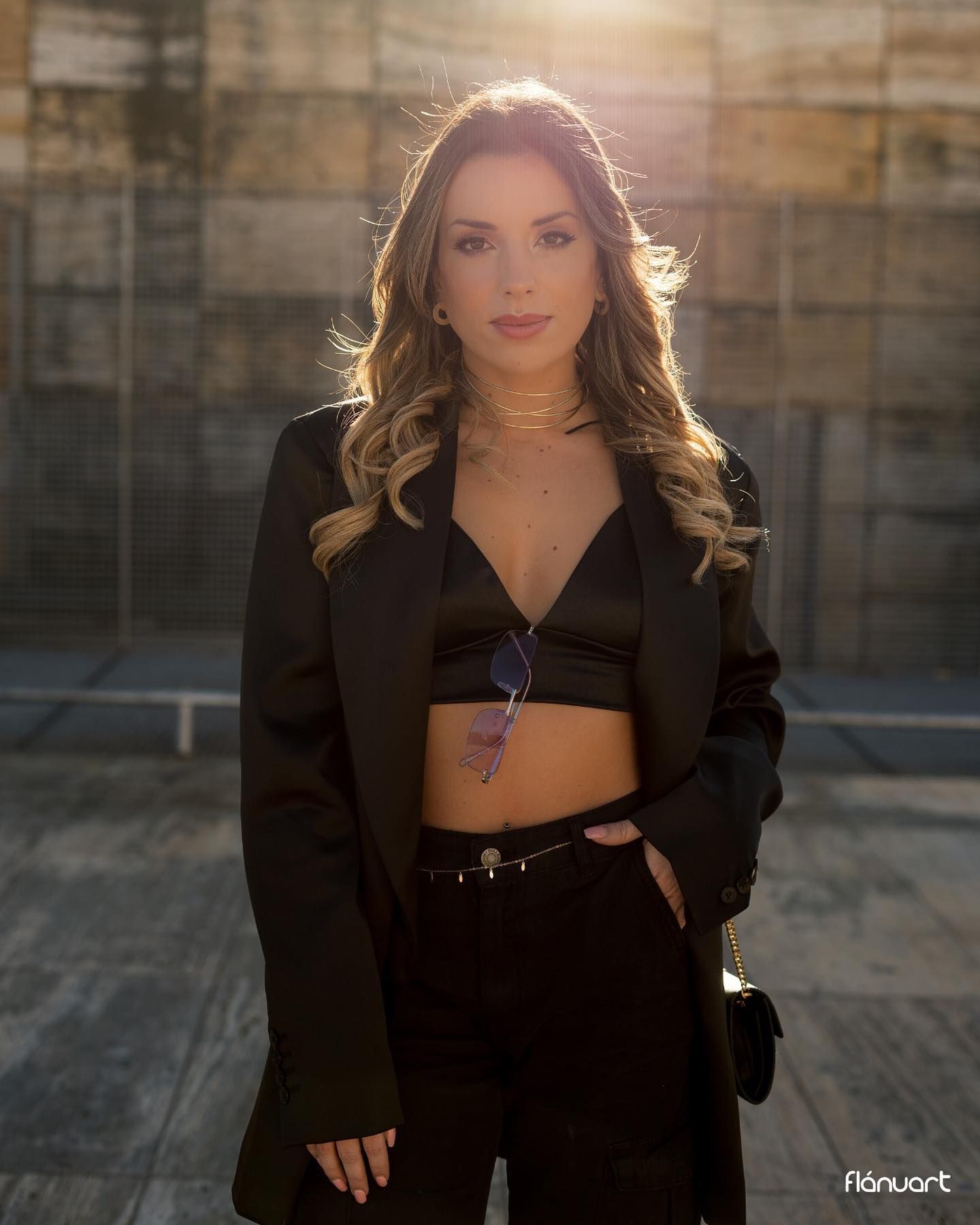 Elegant woman in black blazer and crop top posing outdoors with warm backlit golden hour sunlight.