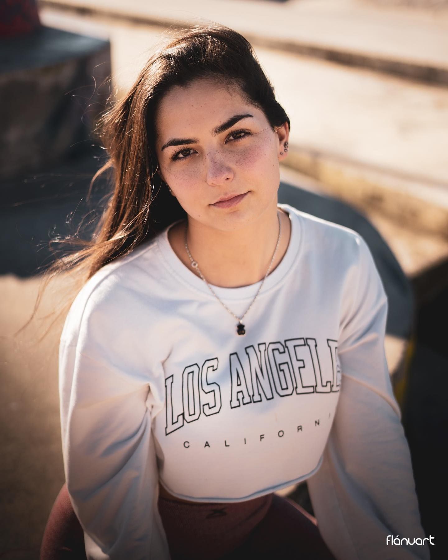 Young woman wearing a Los Angeles California white sweatshirt poses outdoors in warm sunlight.