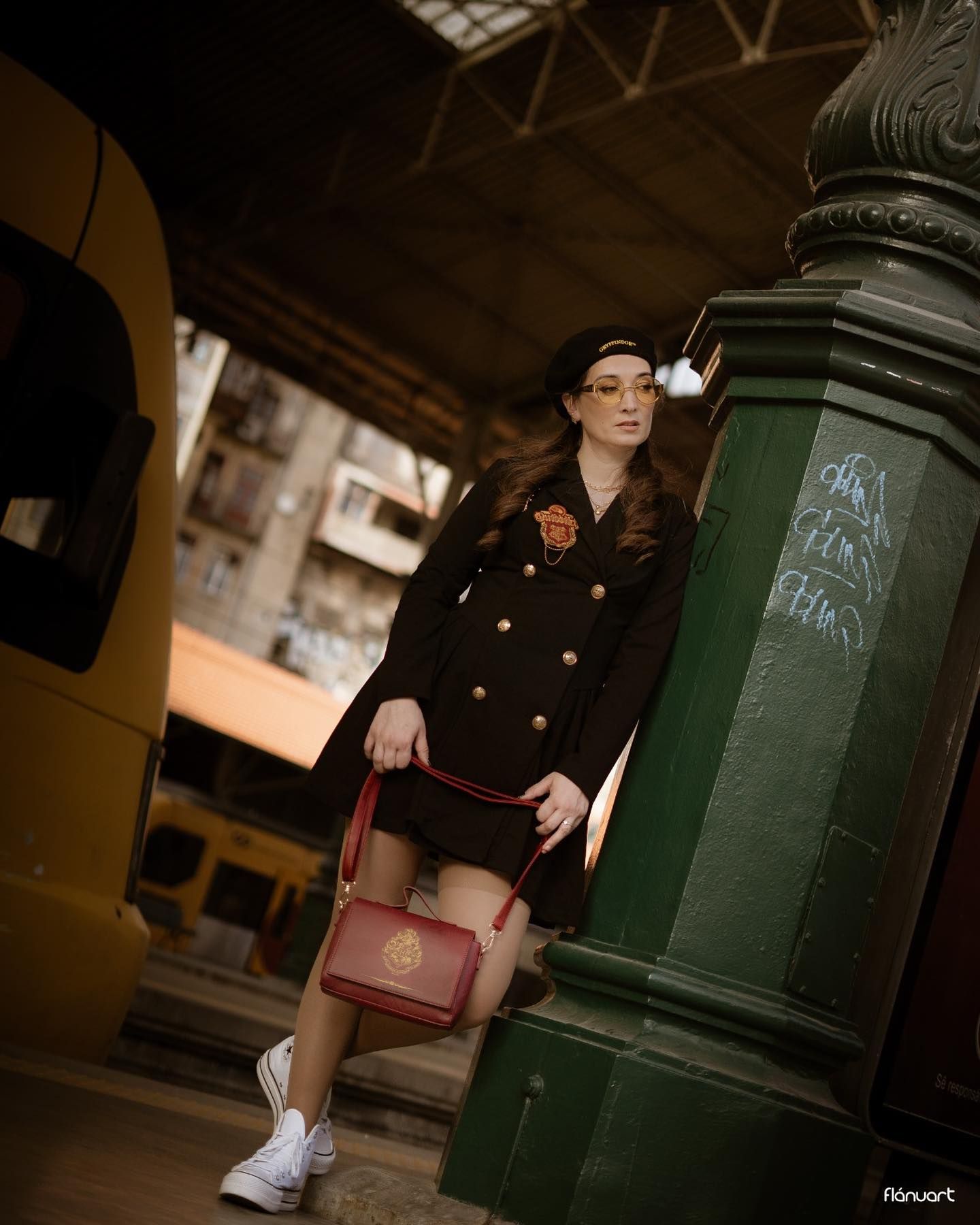 Stylish woman in black military blazer dress with beret and red handbag at vintage train station.