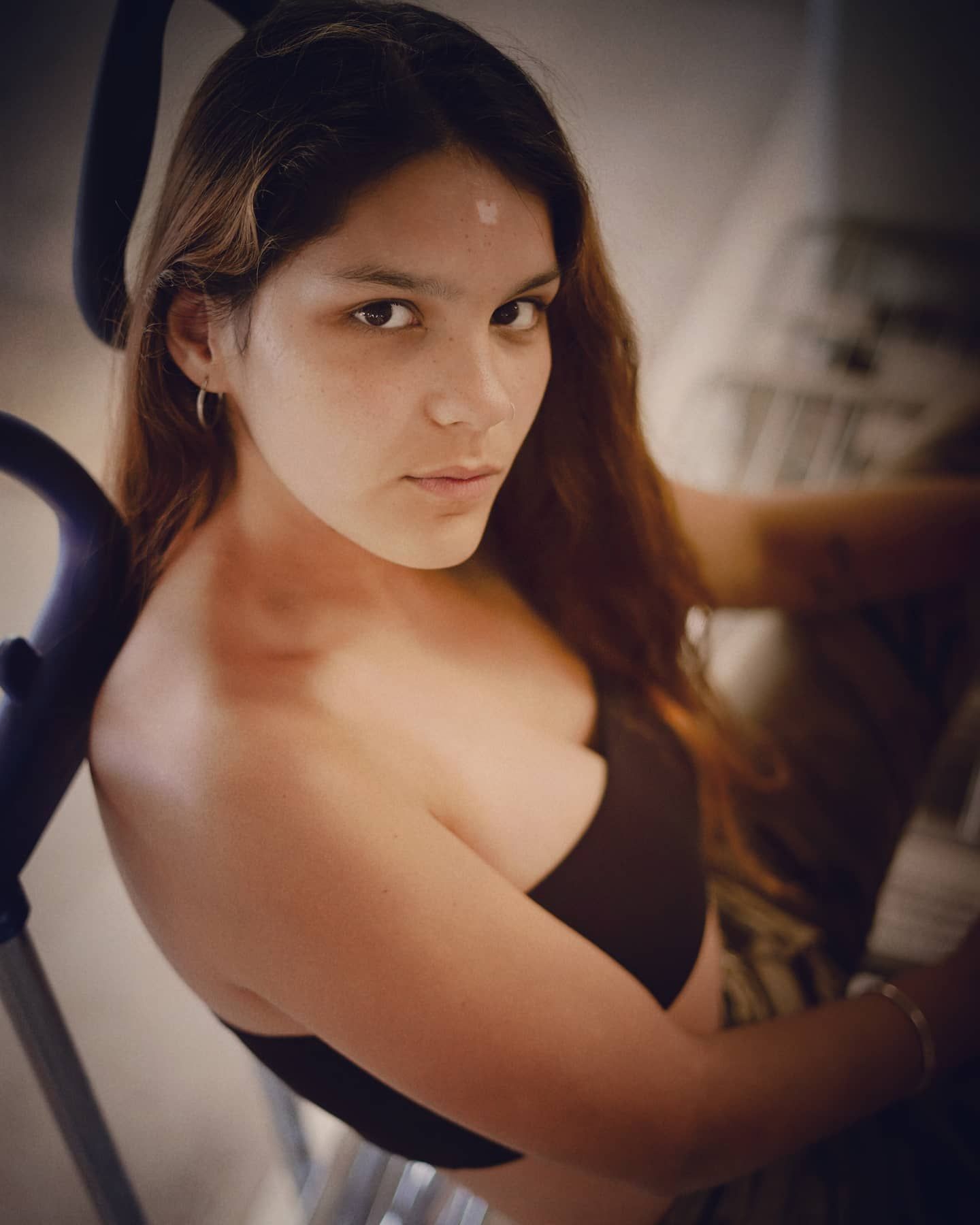 Young woman with long auburn hair posing with a serious expression in warm indoor lighting.