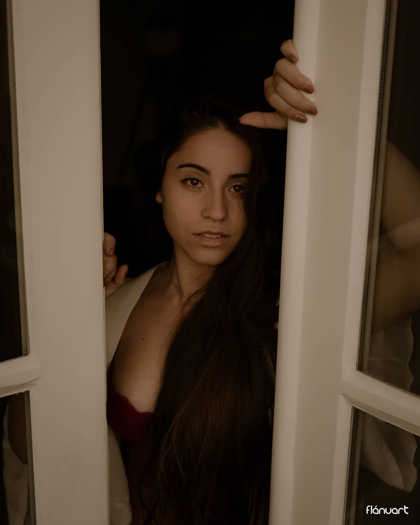 Dark-haired woman in red top peering through white French doors at night.