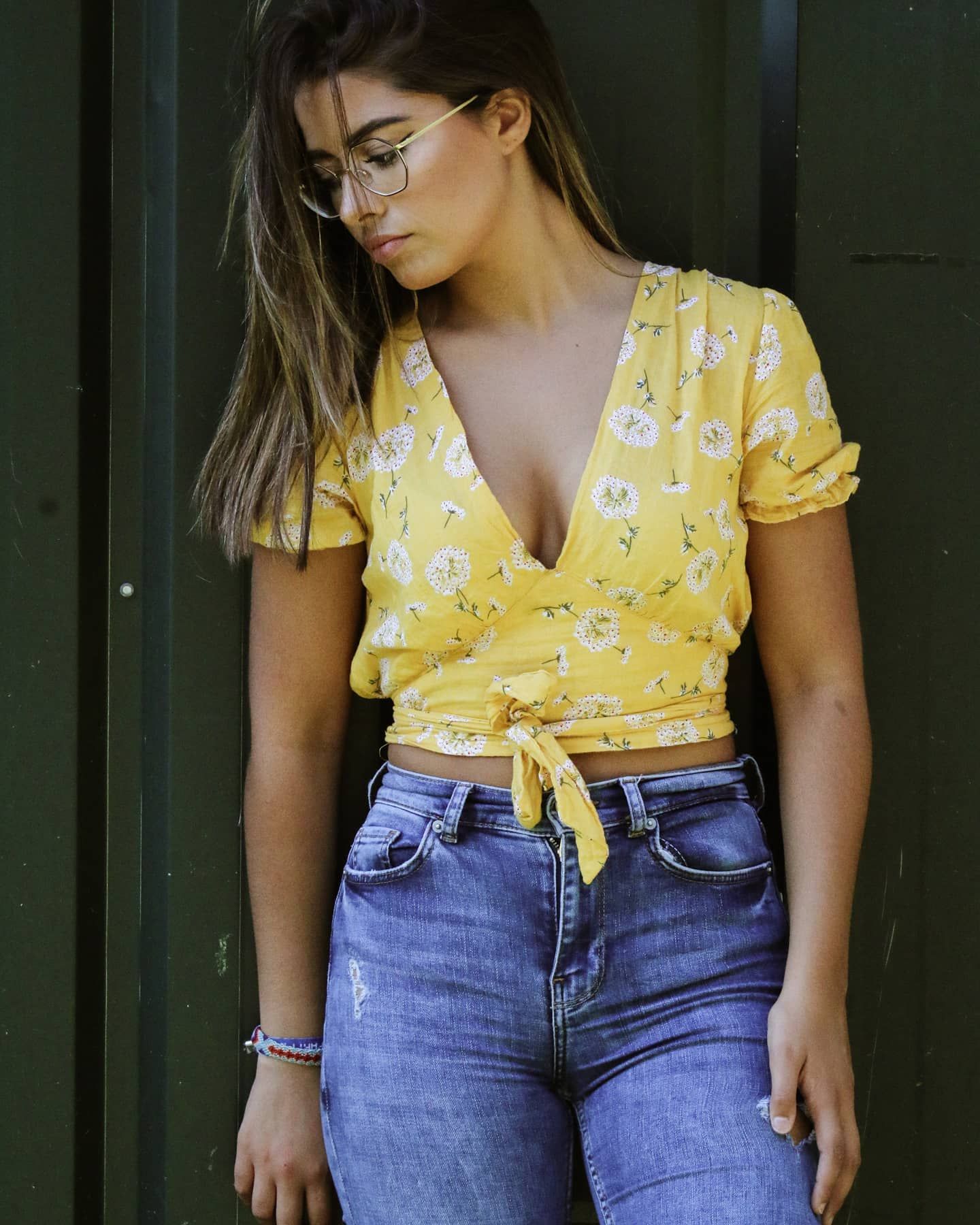 Woman in yellow floral crop top tied at waist paired with blue jeans and glasses.