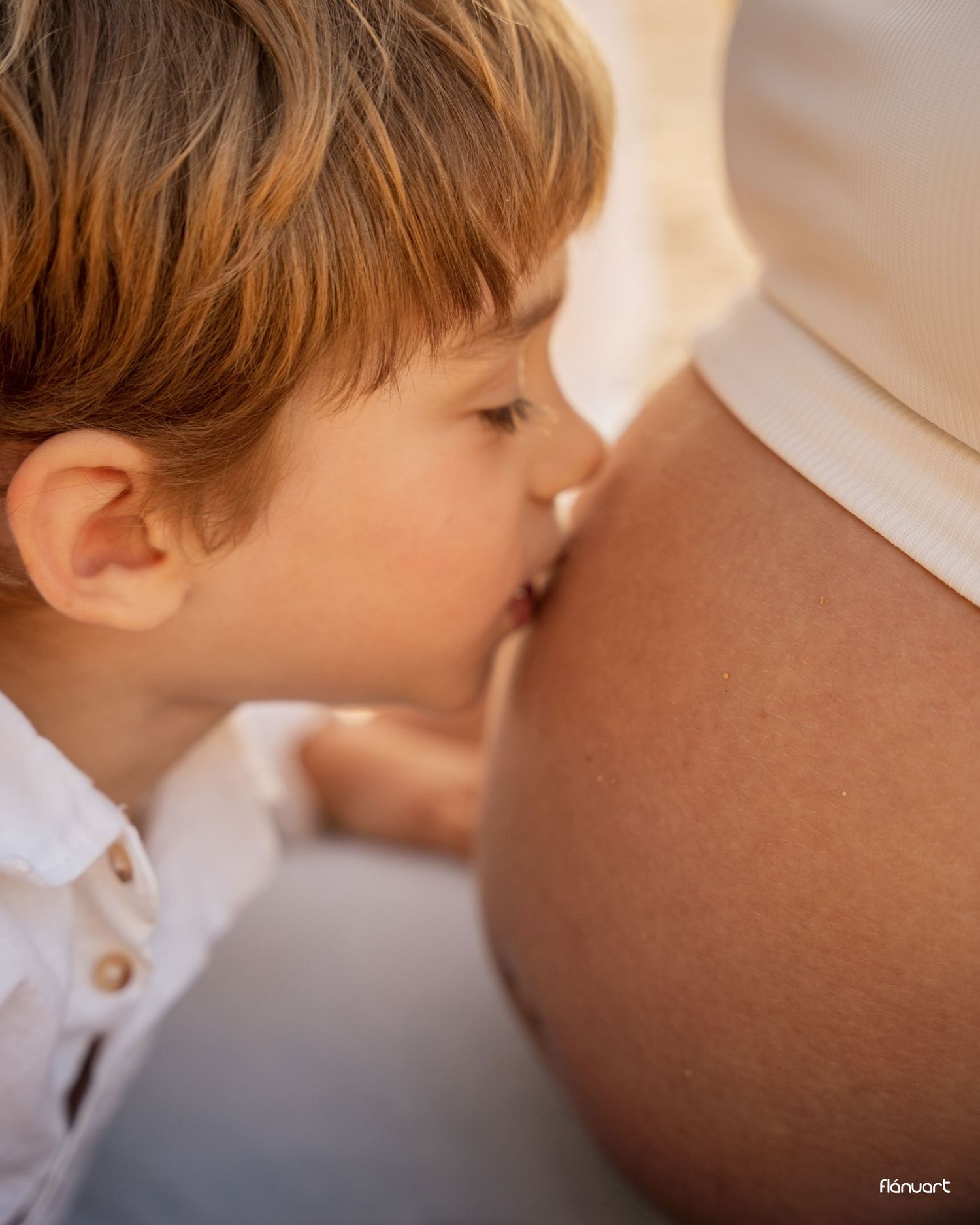 Young child gently kissing mother's pregnant belly in a tender and loving maternity moment.