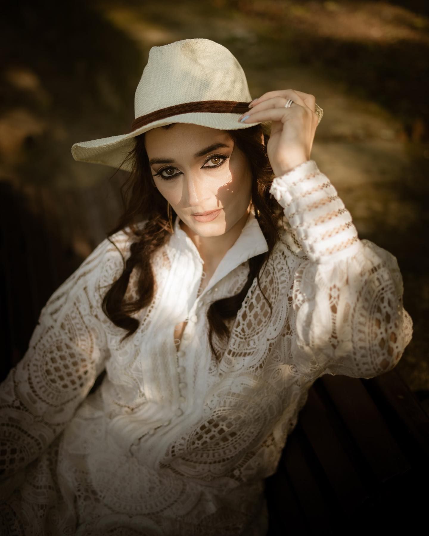 Young woman in white lace blouse and cream cowboy hat posing outdoors in warm golden light.