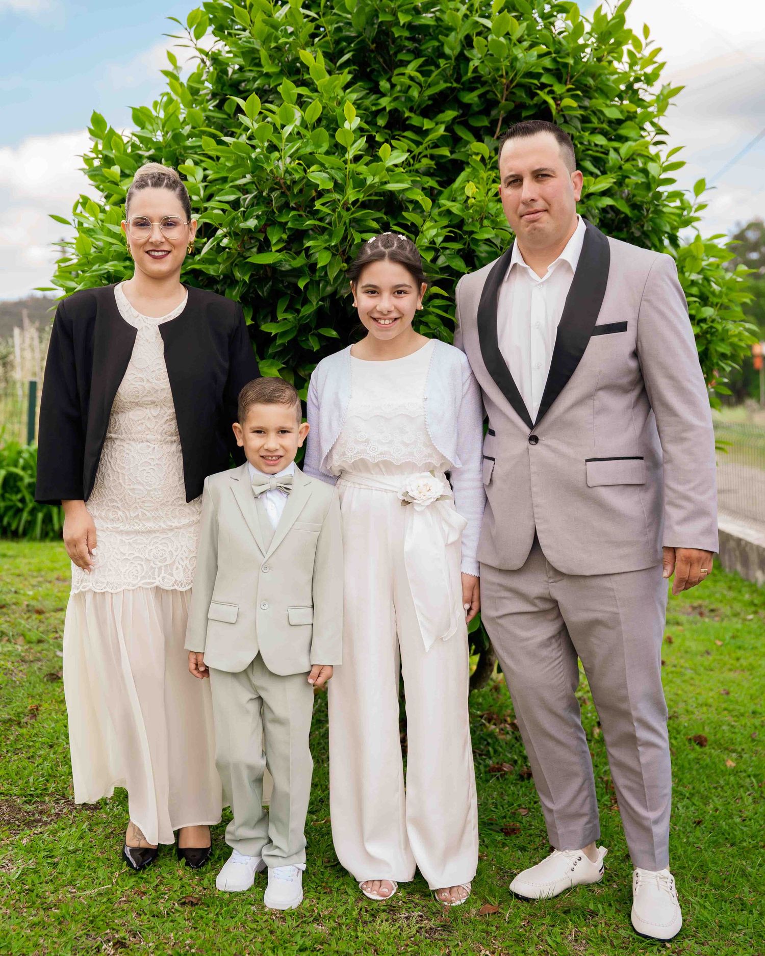 A family of four poses outdoors in formal attire for a First Communion celebration.