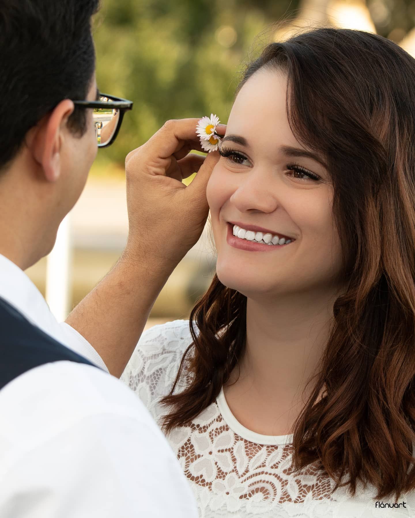 Young woman smiling as man places a daisy flower in her hair during an outdoor photo session.