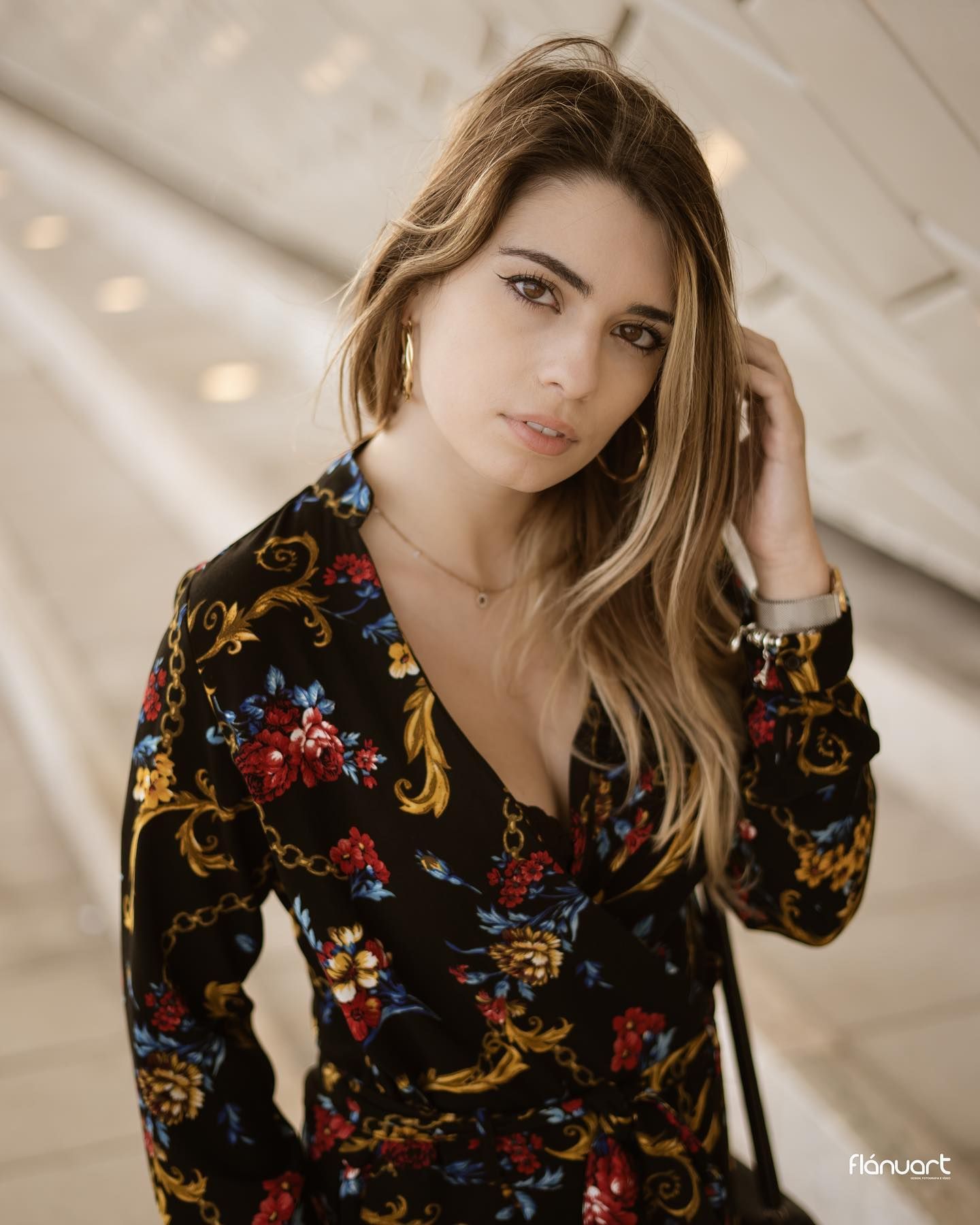 Woman in floral wrap dress with golden highlights posing in a modern architectural setting.