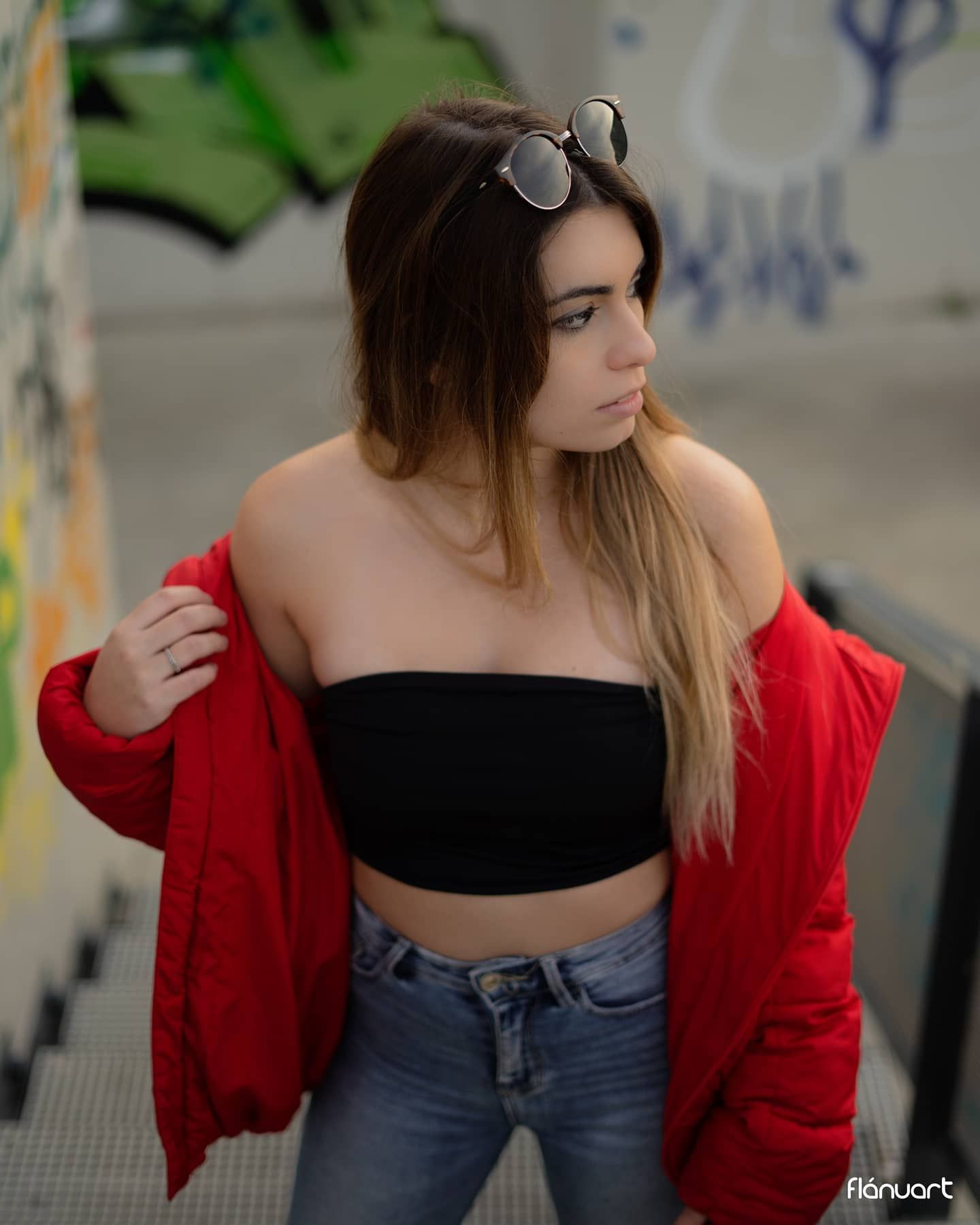 Stylish young woman in red jacket and black crop top posing in front of a graffiti wall.