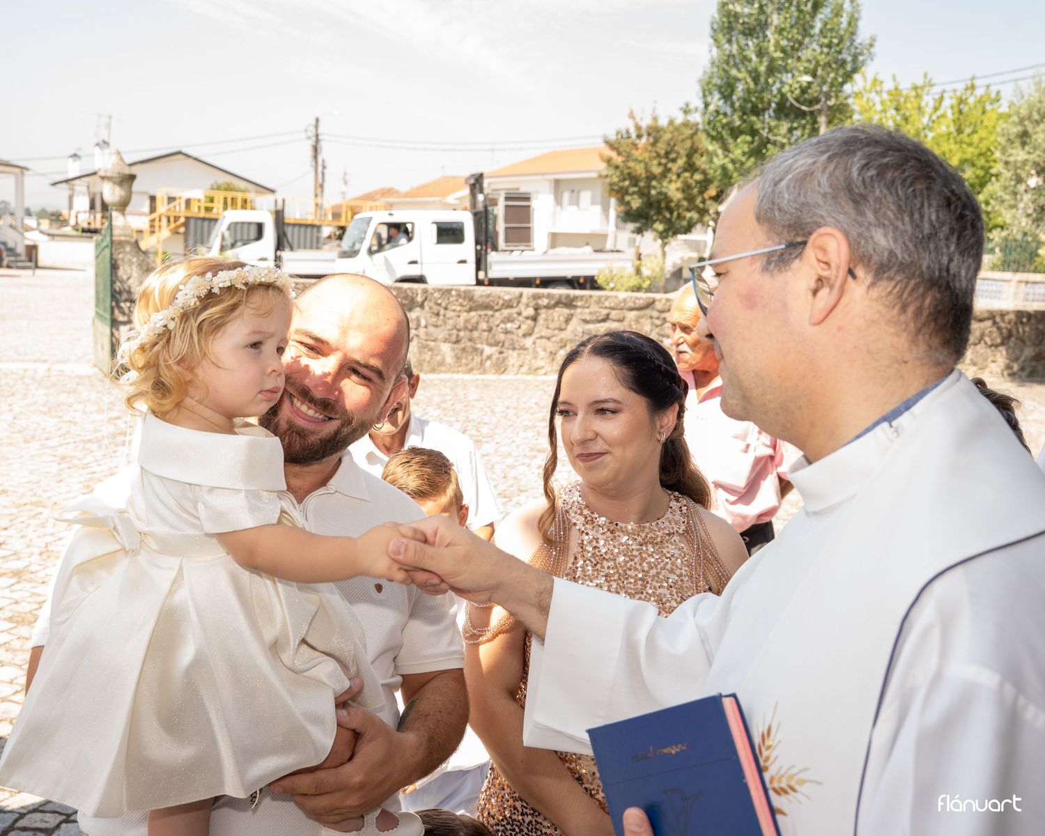 A priest greets a family during a baptism ceremony, with a father holding a child in white.