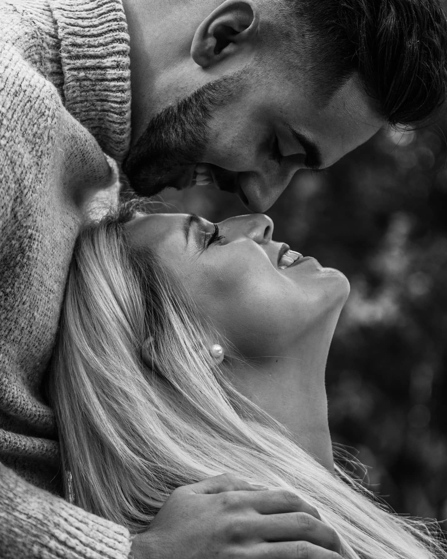 Black and white intimate close-up of couple leaning in for a kiss, woman with blonde hair and pearl earring.