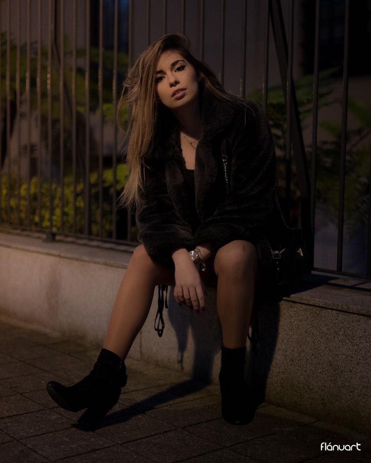 Young woman in an all-black outfit sitting on steps at night in an urban setting.