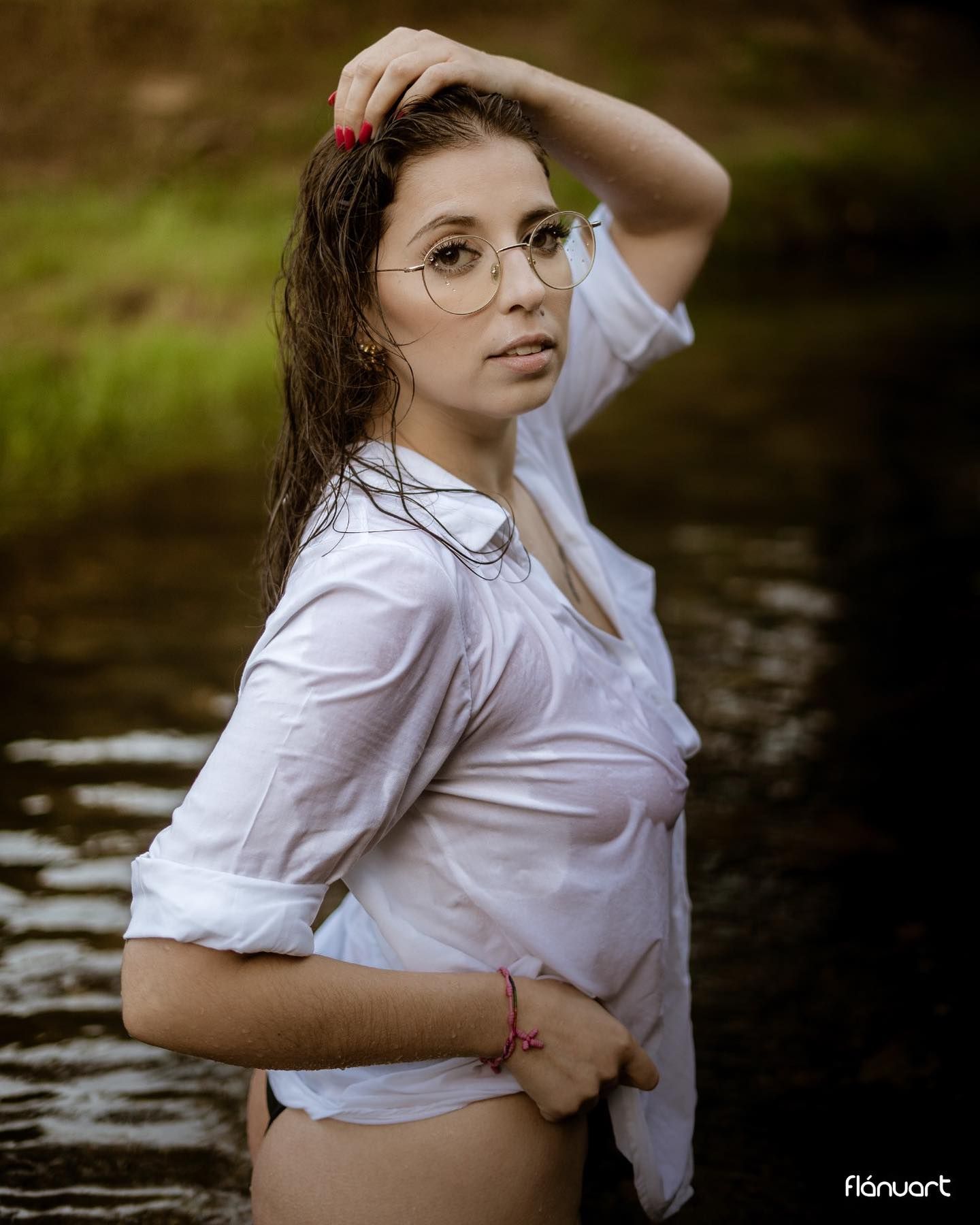 Woman in wet white shirt and round glasses poses in river.