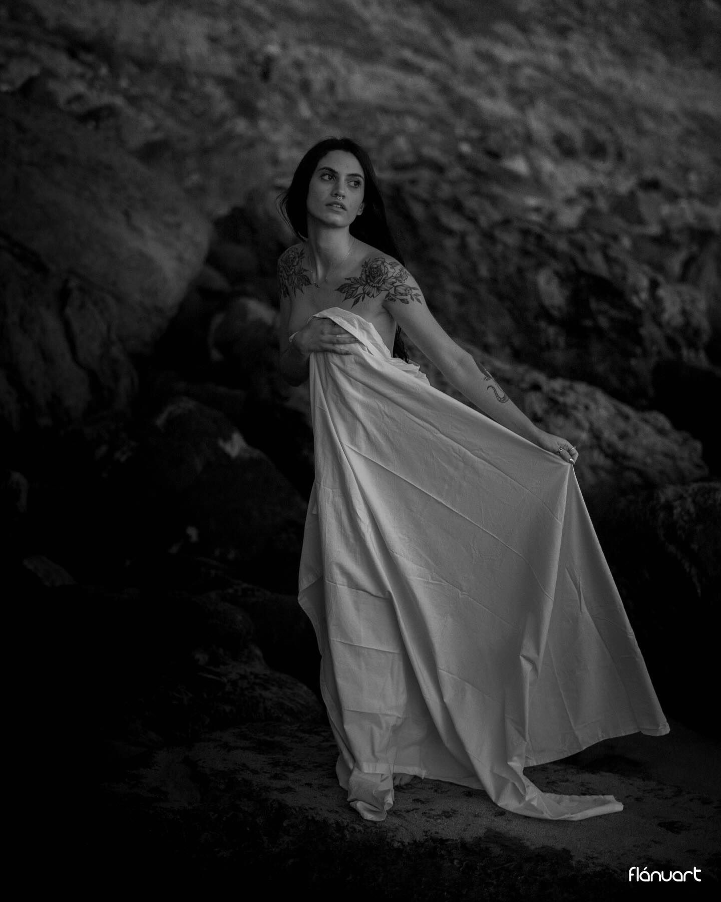 Black and white photo of woman in white dress among rocks.