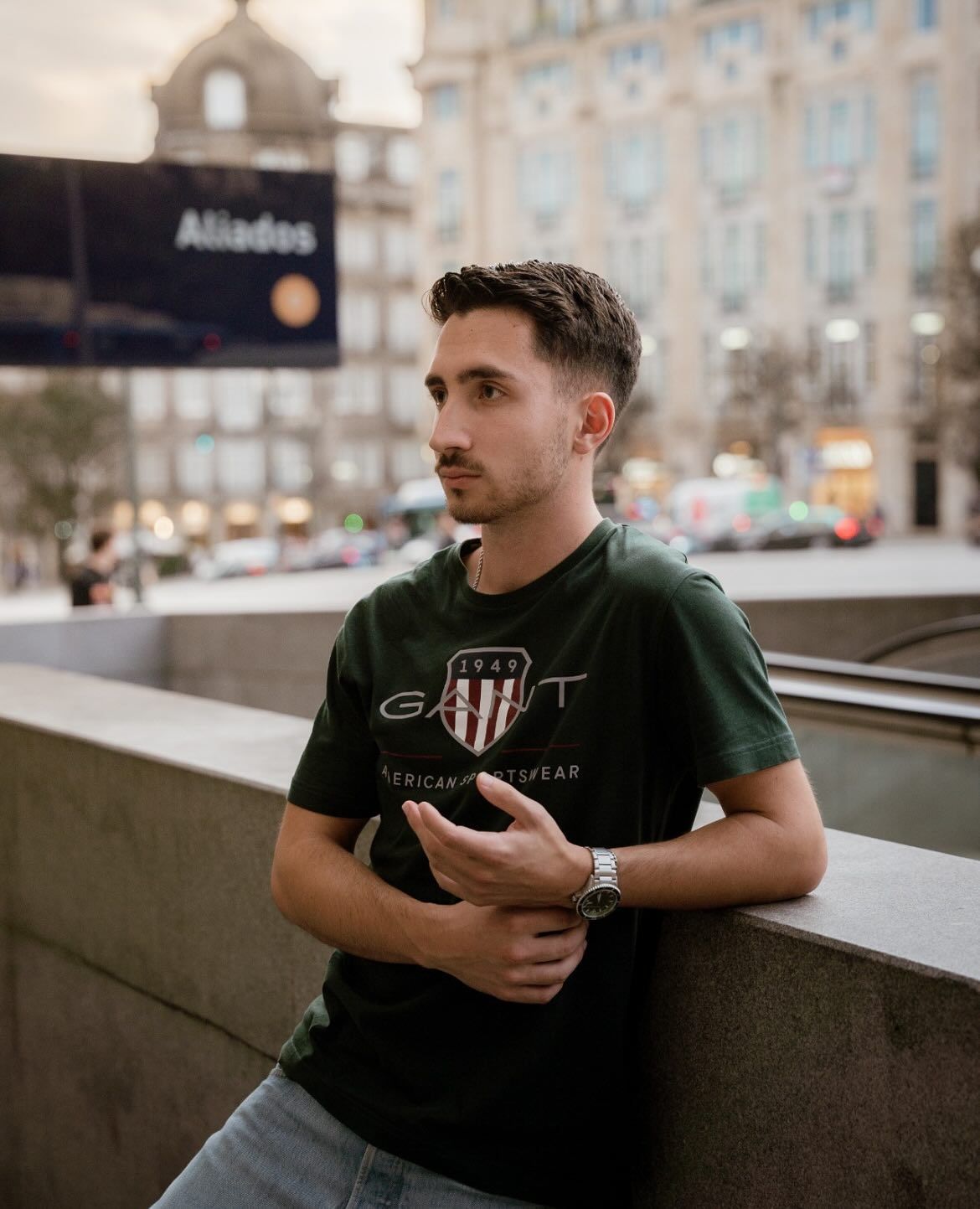 Young man in green Gant t-shirt leaning on a wall at Aliados square in Porto.