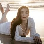 Young woman in white lace top lying on reflective wet beach at sunset.