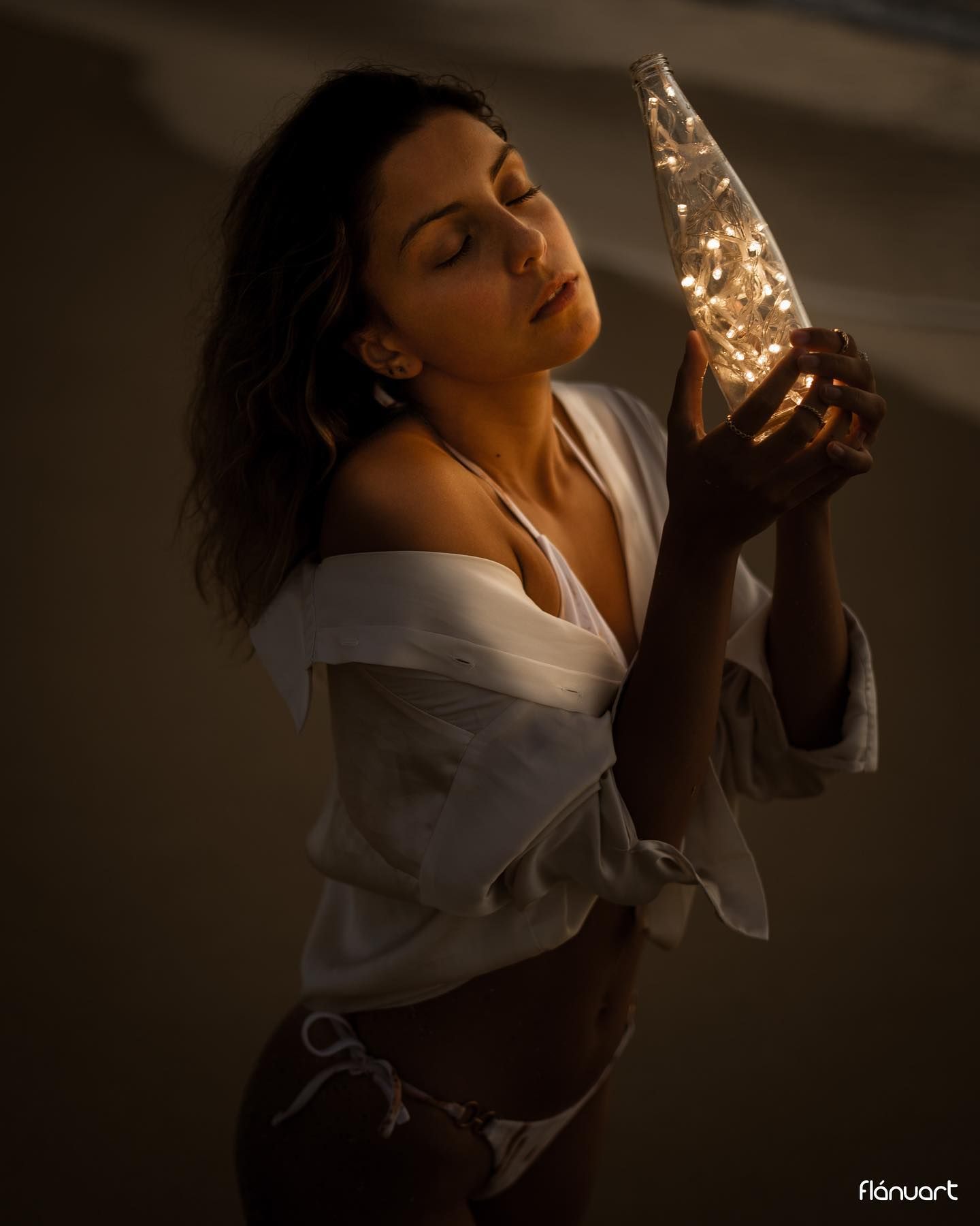 Woman holding glowing bottle with fairy lights indoors.