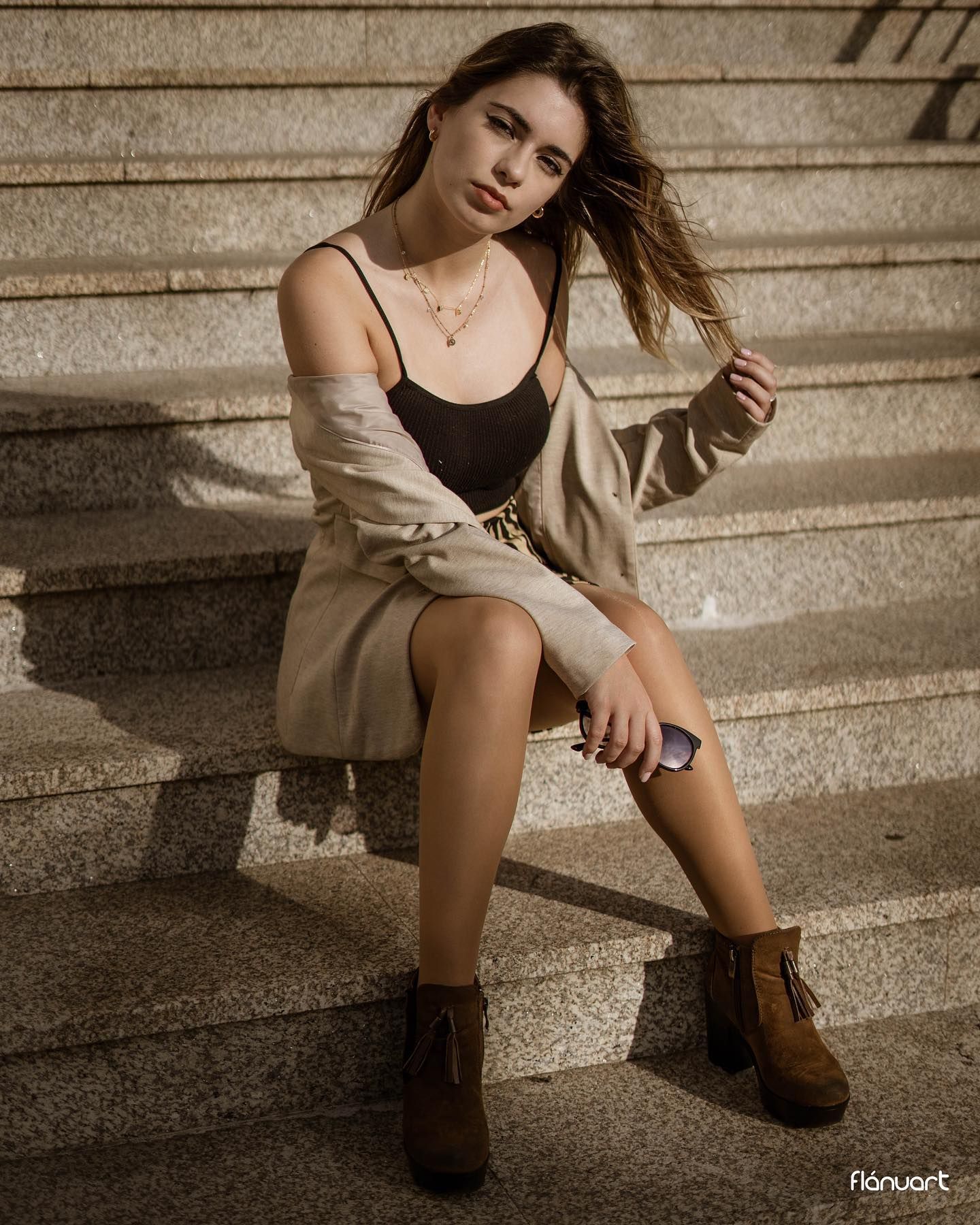 Young woman in beige cardigan and black bodysuit sitting on stone steps in warm light.