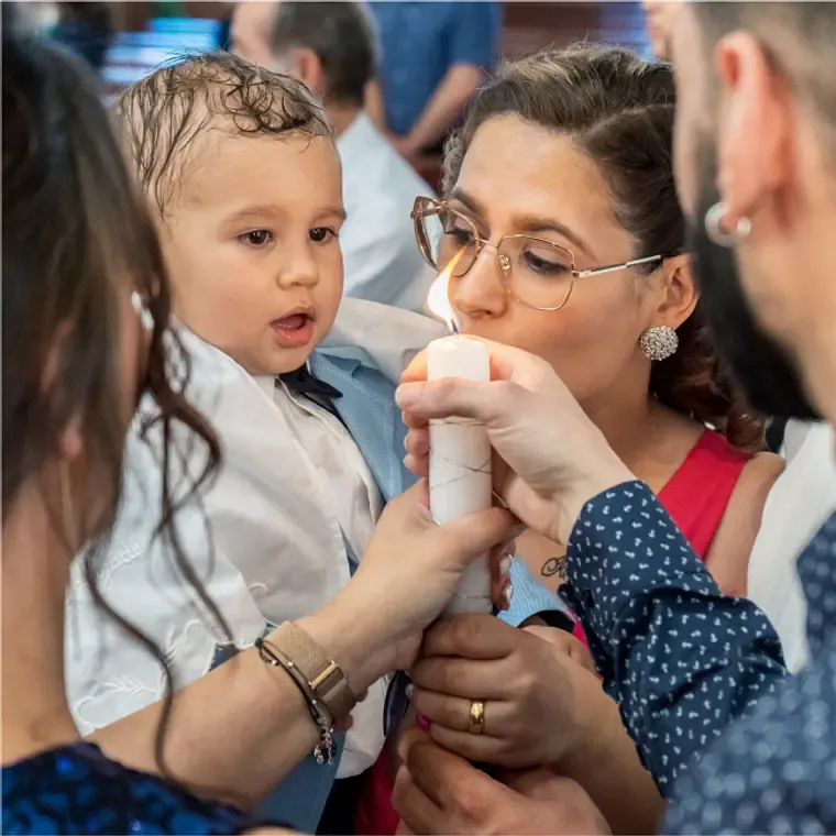 Woman helping toddler boy interact with a candle during a baptism ceremony.