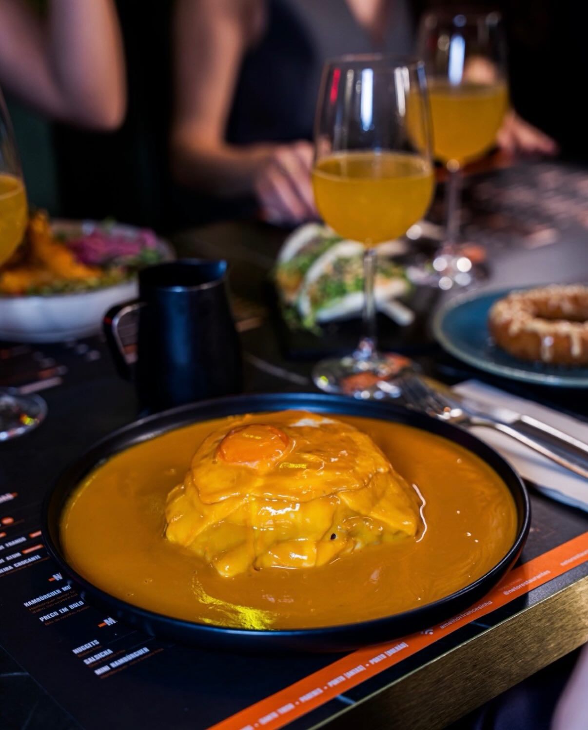Traditional Portuguese Francesinha dish in rich sauce served with a glass of orange juice.
