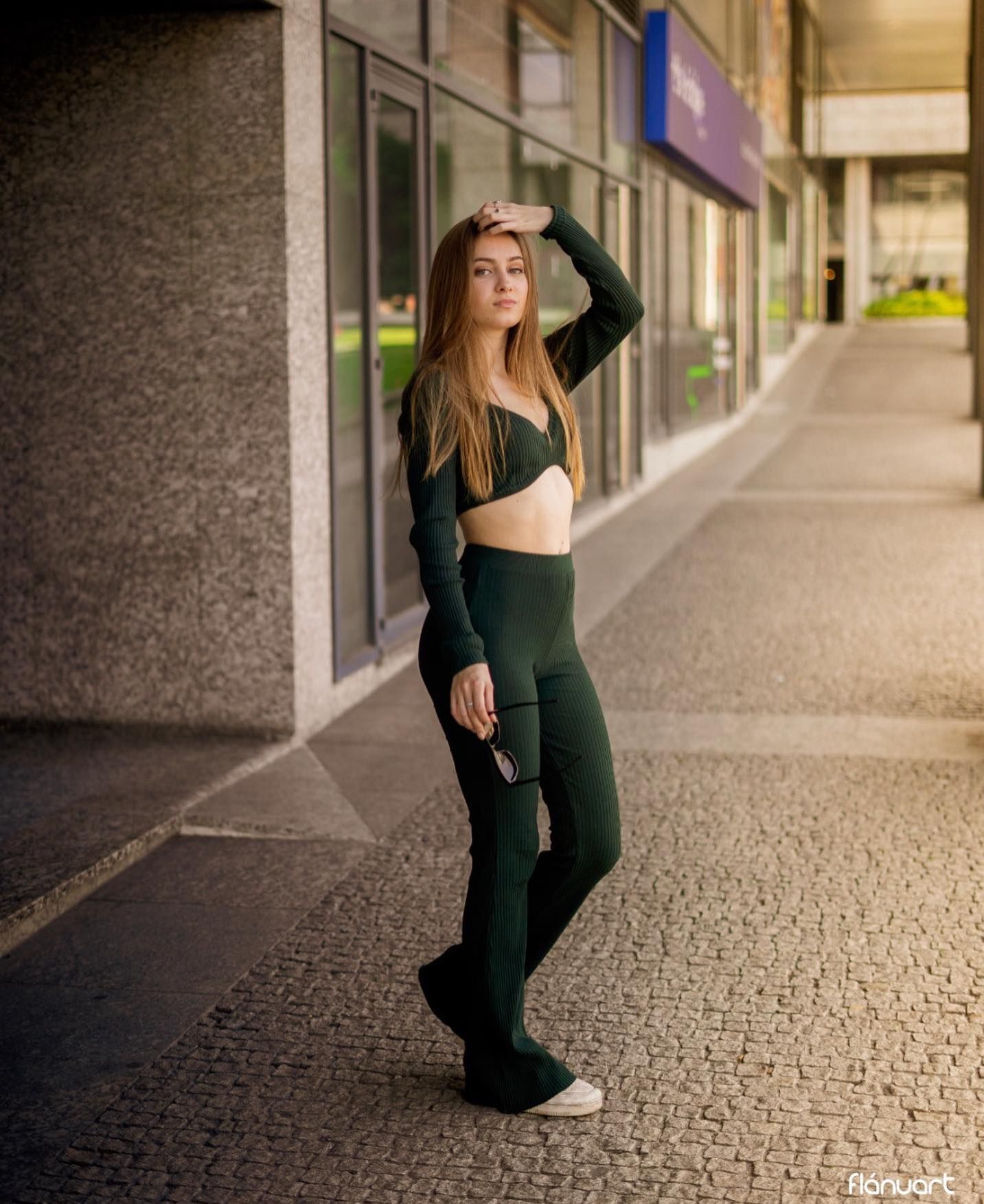 Slim woman in green crop top and flare pants posing on urban walkway.