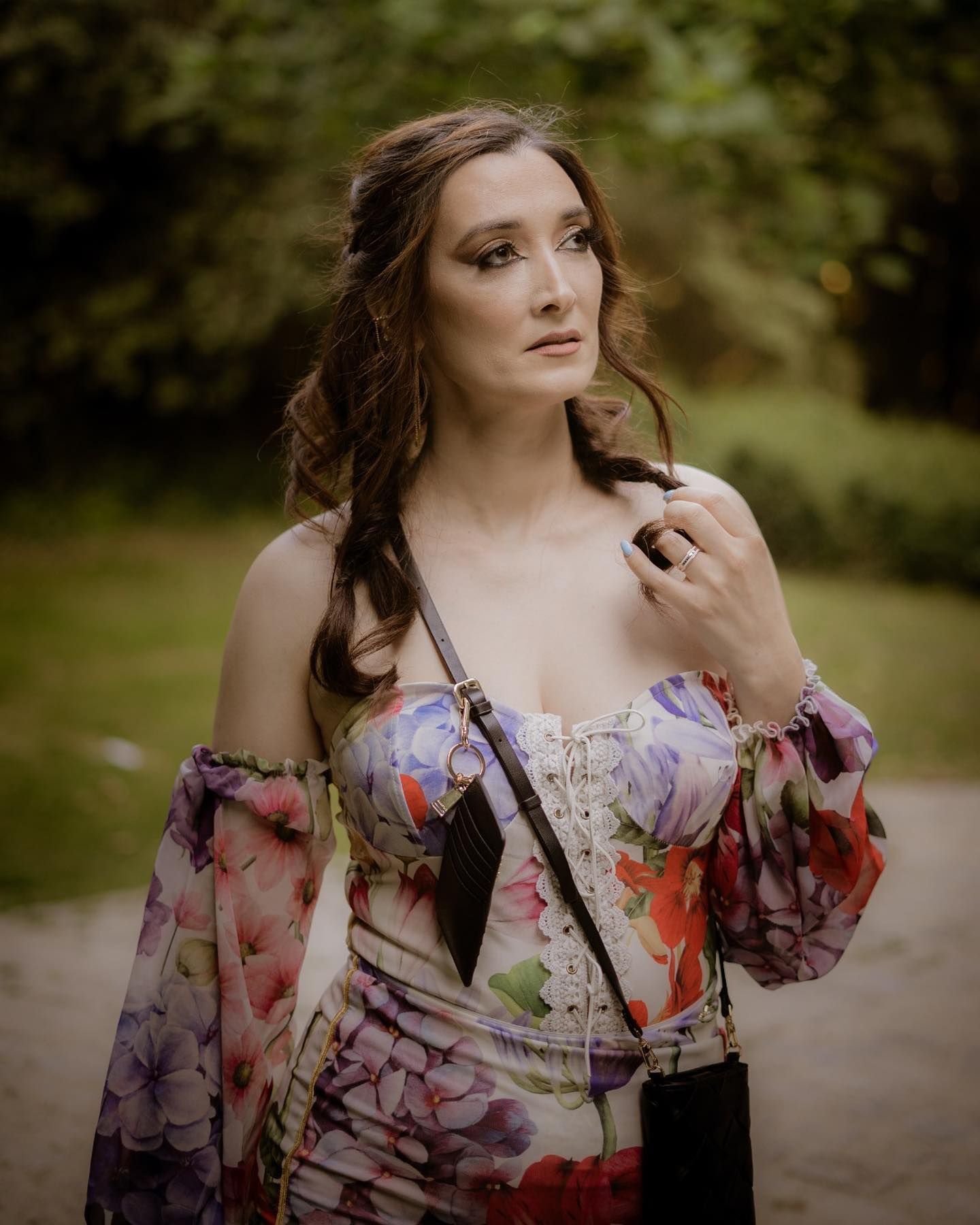 Elegant woman in floral off-shoulder dress with corset detail posing in lush green outdoor setting.