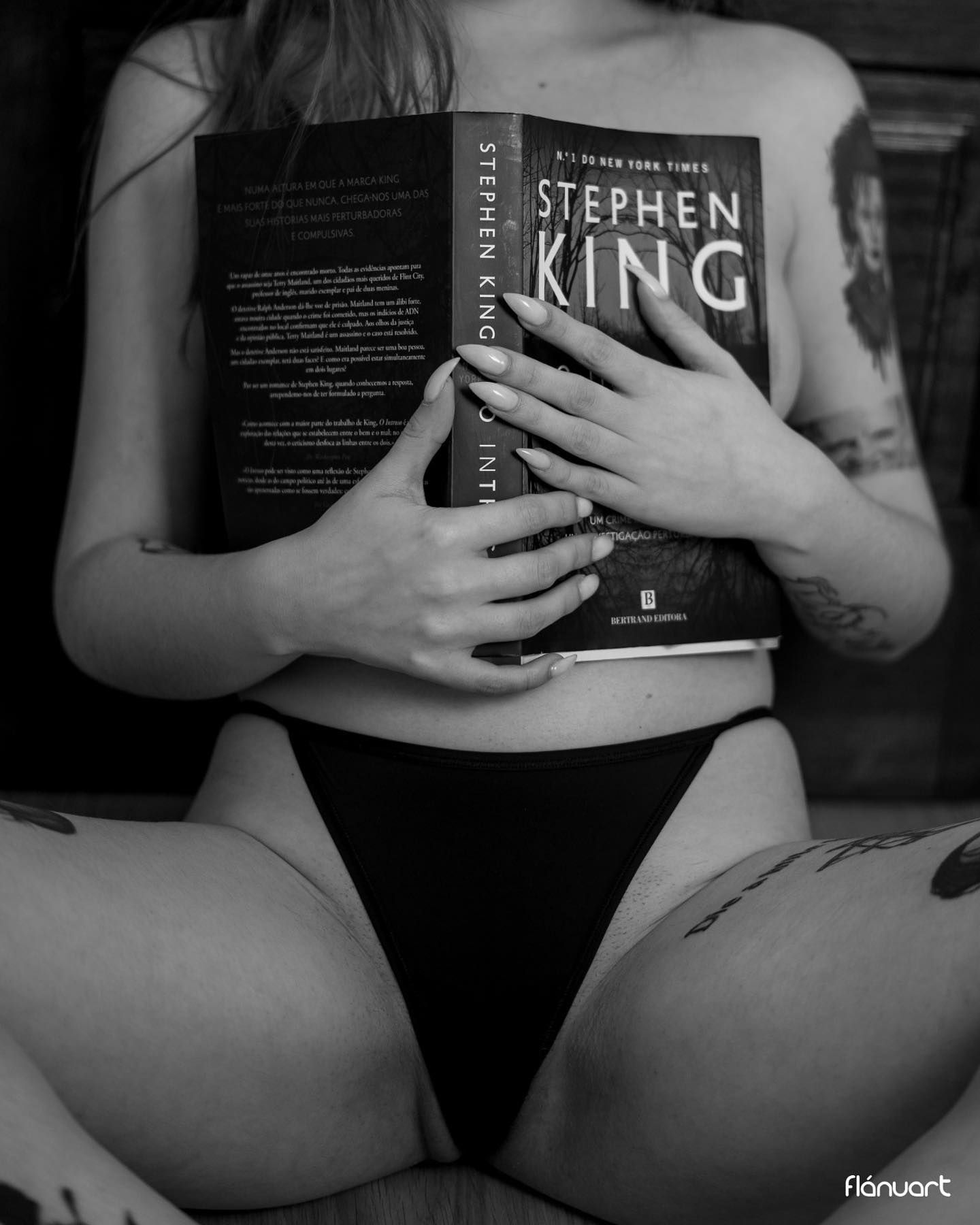 Black and white photo of tattooed woman holding a Stephen King book while seated in lingerie.