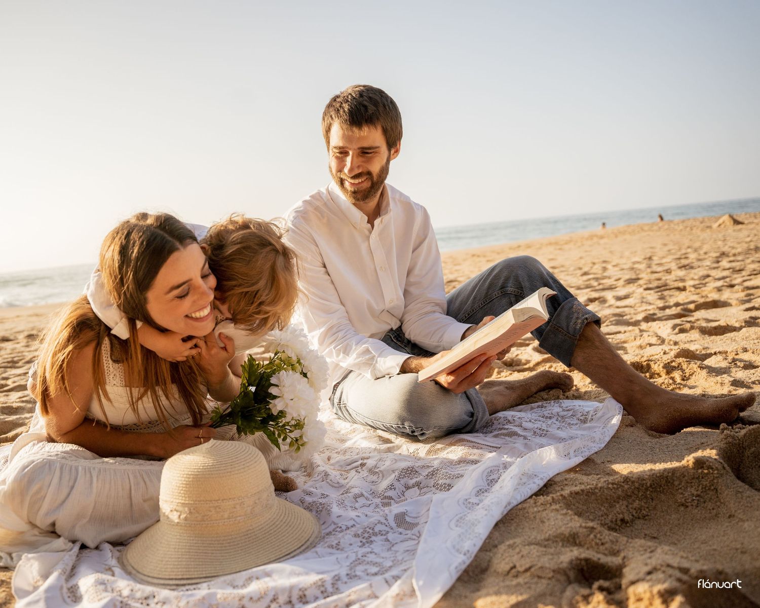 Happy family relaxing on beach blanket at sunset, reading and sharing tender moments.