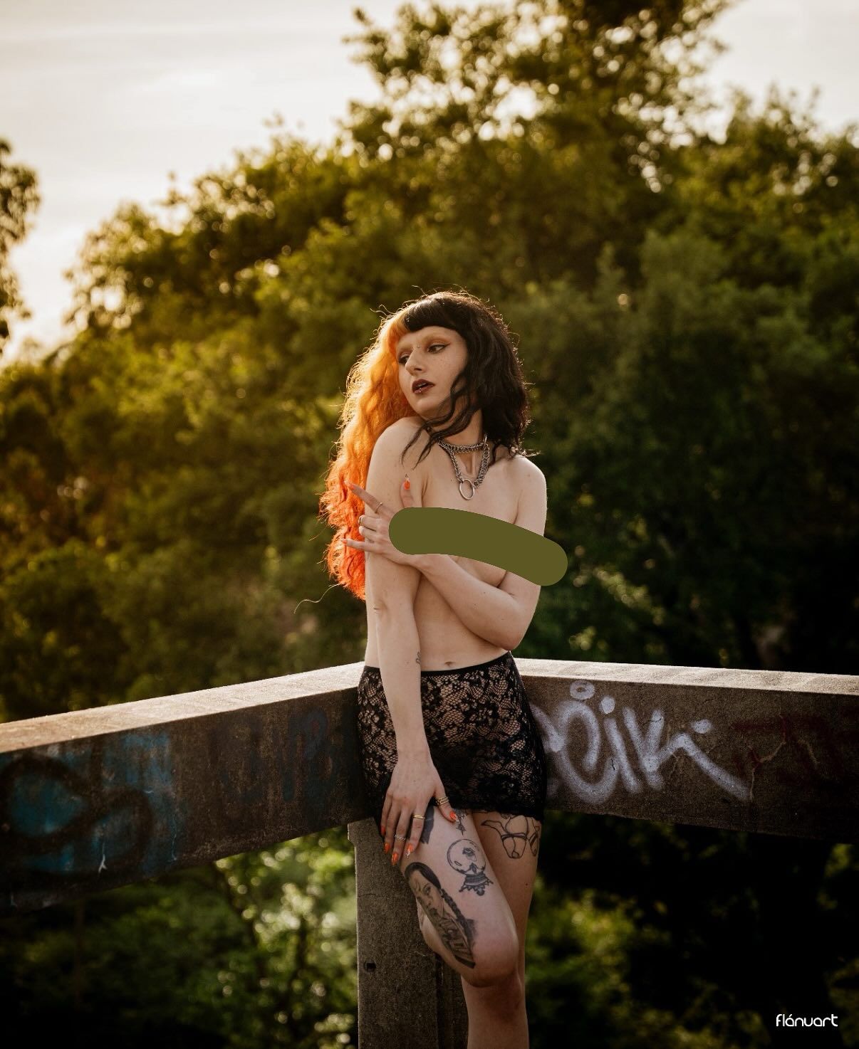 Woman with red hair posing topless at sunset on graffiti bridge wearing lace shorts with tattoos.