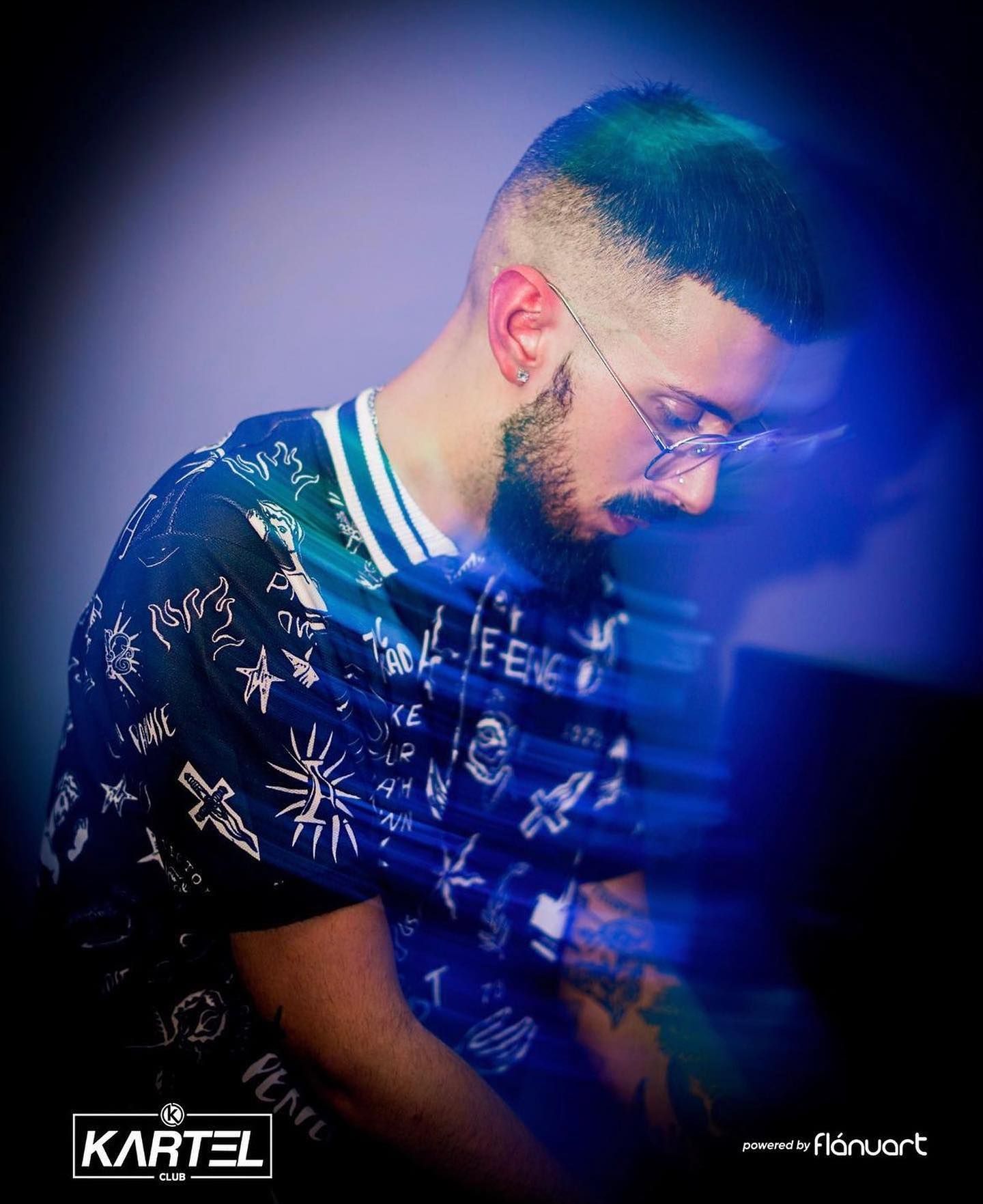 DJ with glasses and beard wearing a graphic tee, focused on mixing music at Kartel Club.