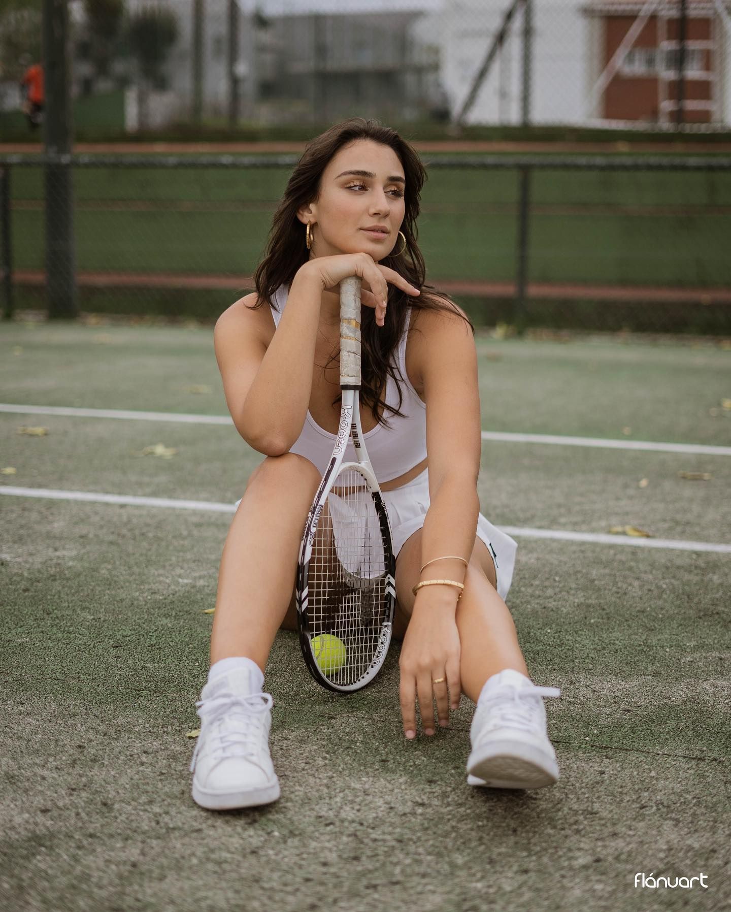Athletic woman in white sports outfit sitting on tennis court with racket.