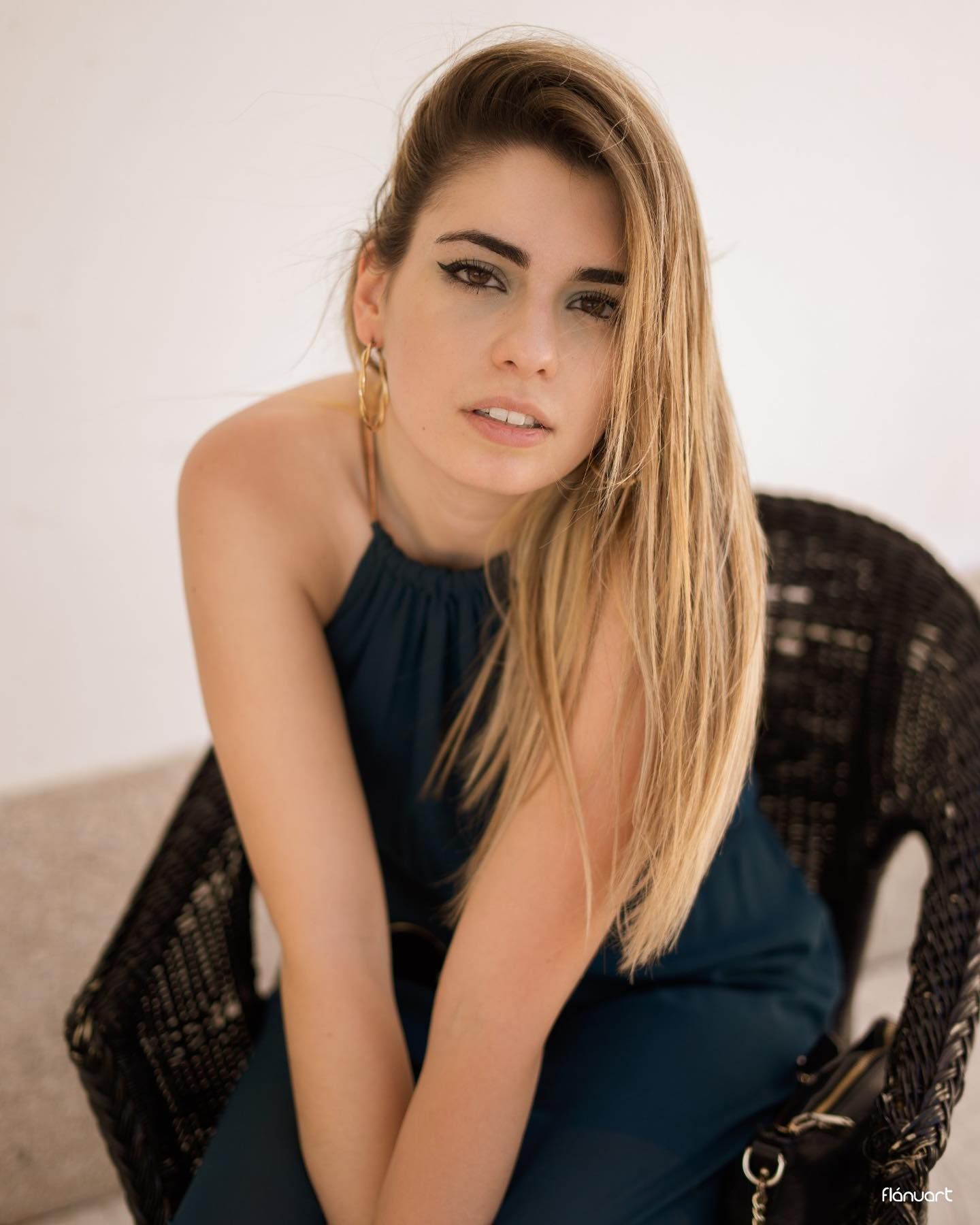 Elegant woman in teal dress with gold hoop earrings sits posed against a white background.