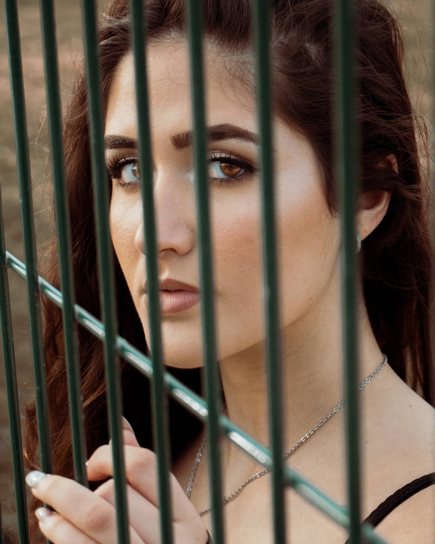 Close-up portrait of brunette woman with striking eyes peering through green metal fence.