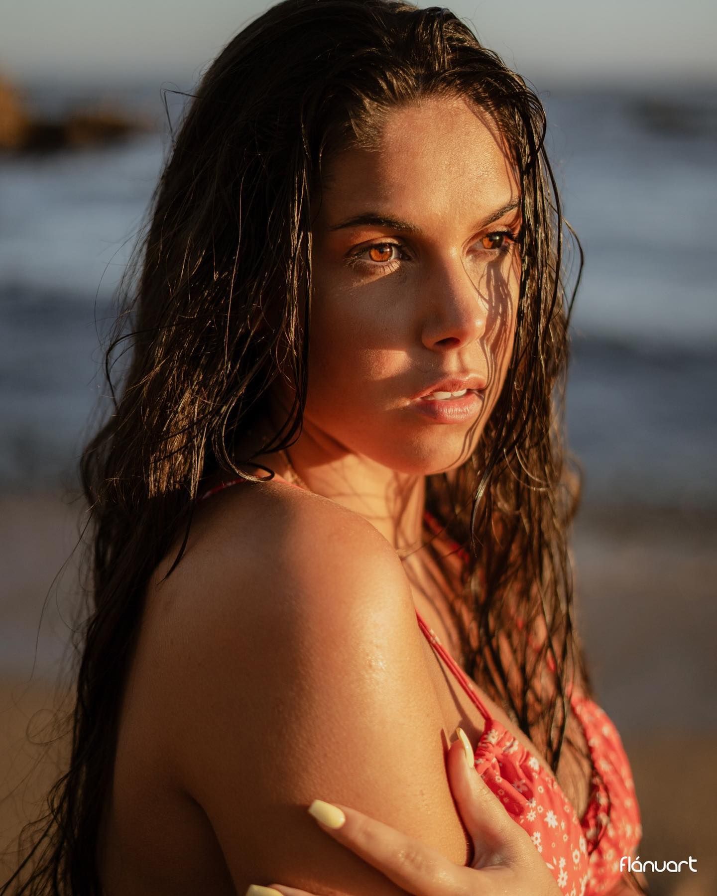 Woman with wet dark hair in pink bikini posing on beach at golden hour.