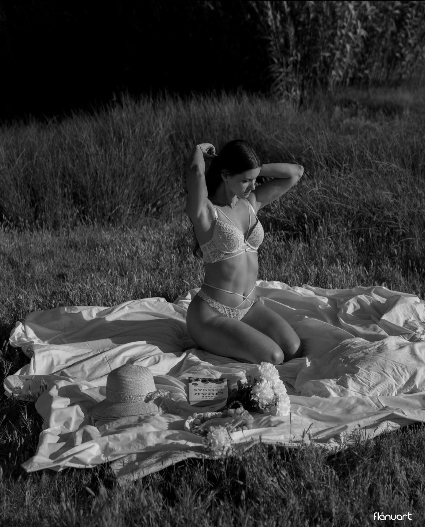 Black and white photo of woman in lingerie kneeling on blanket in grassy outdoor setting.