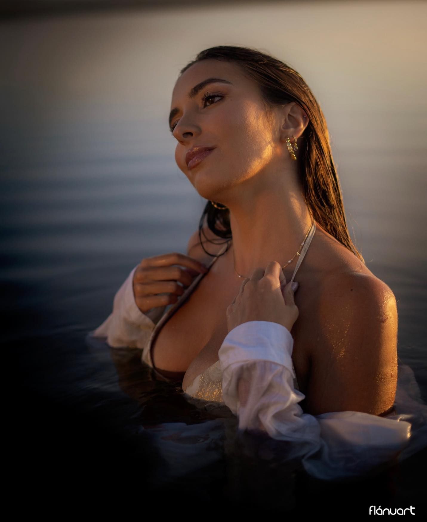 Woman in wet white shirt emerging from water at golden hour sunset.