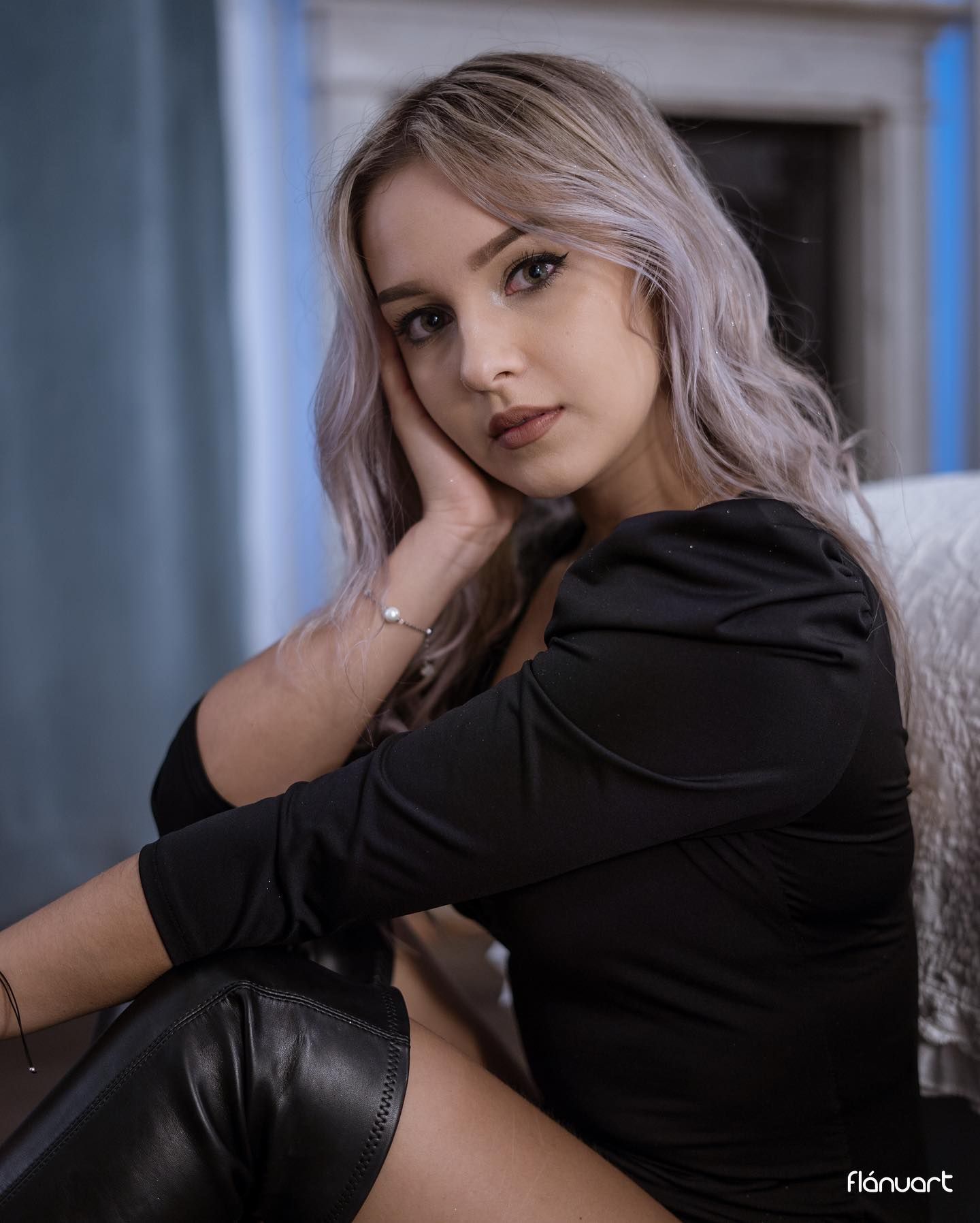 Young woman with silver hair in black outfit poses against blue interior backdrop.