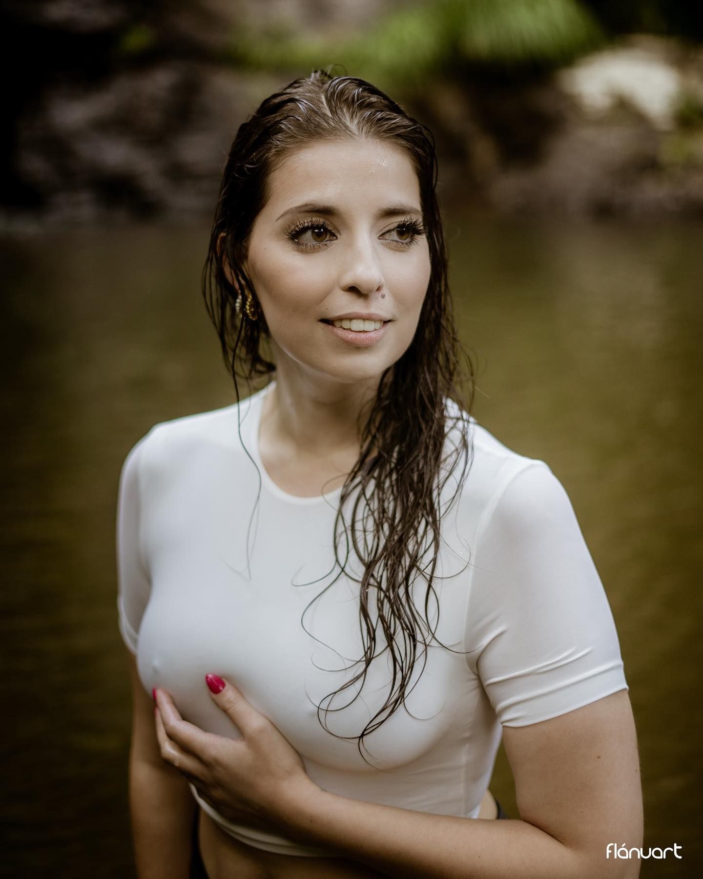 Woman in wet white t-shirt standing in natural pool surrounded by lush green foliage.