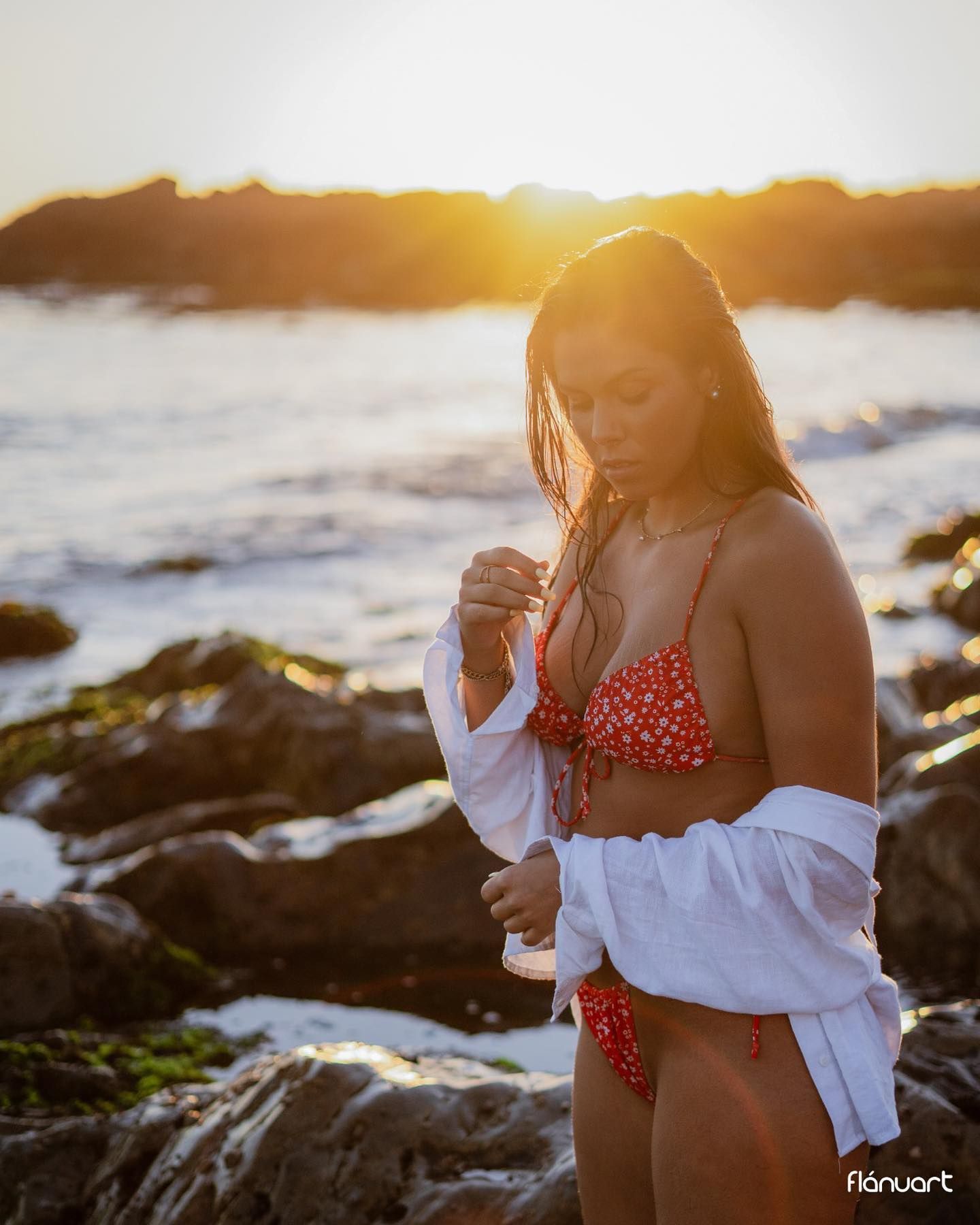 Woman in red floral bikini at rocky beach during sunset.