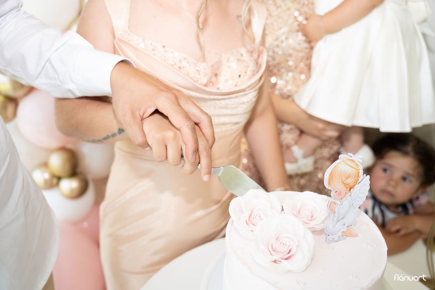Bride and groom cutting a white wedding cake adorned with pink roses and a figurine topper at a reception.